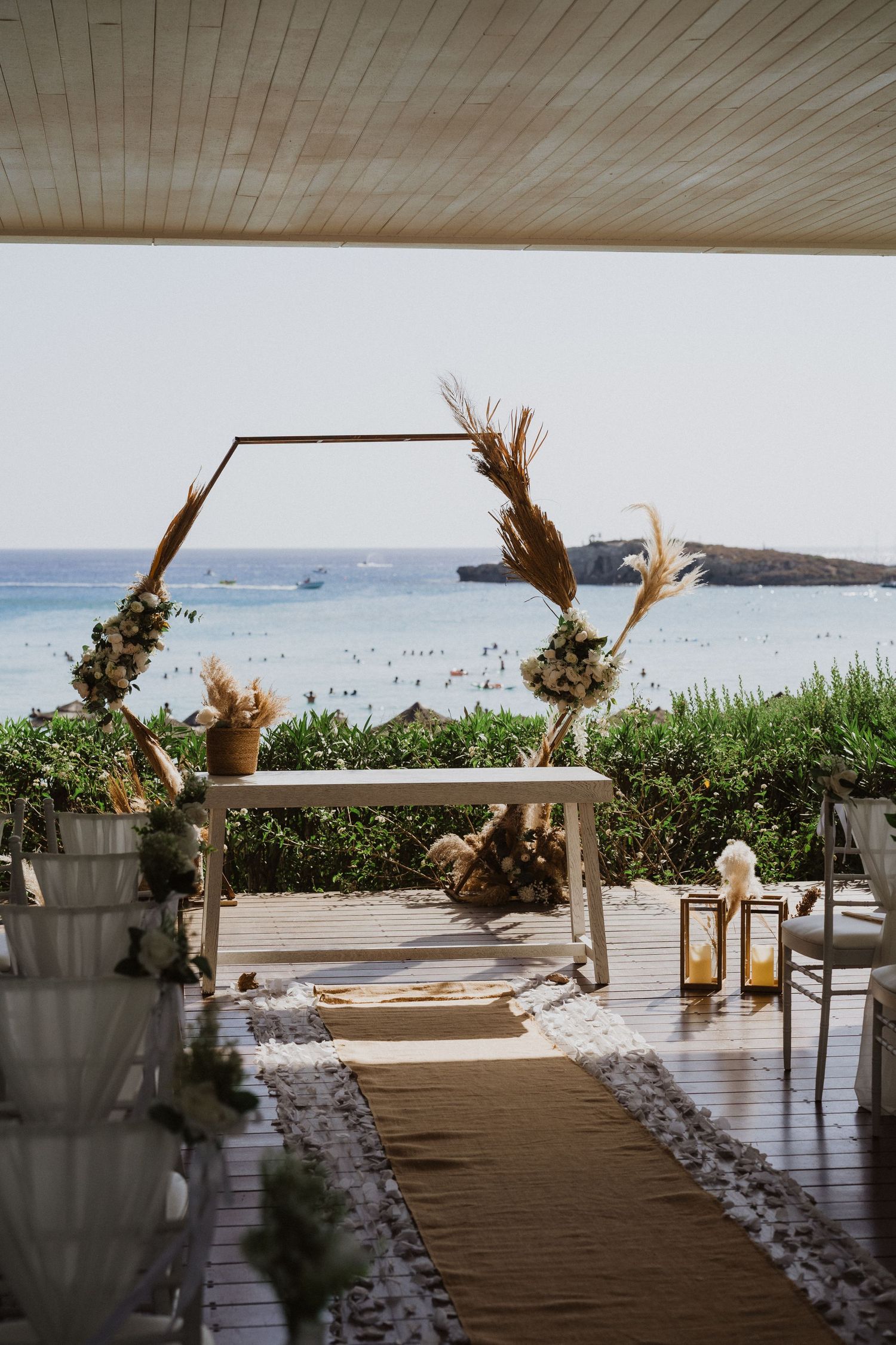 Rustic wedding arch decorated with dried flowers frames an ocean view on a covered deck.