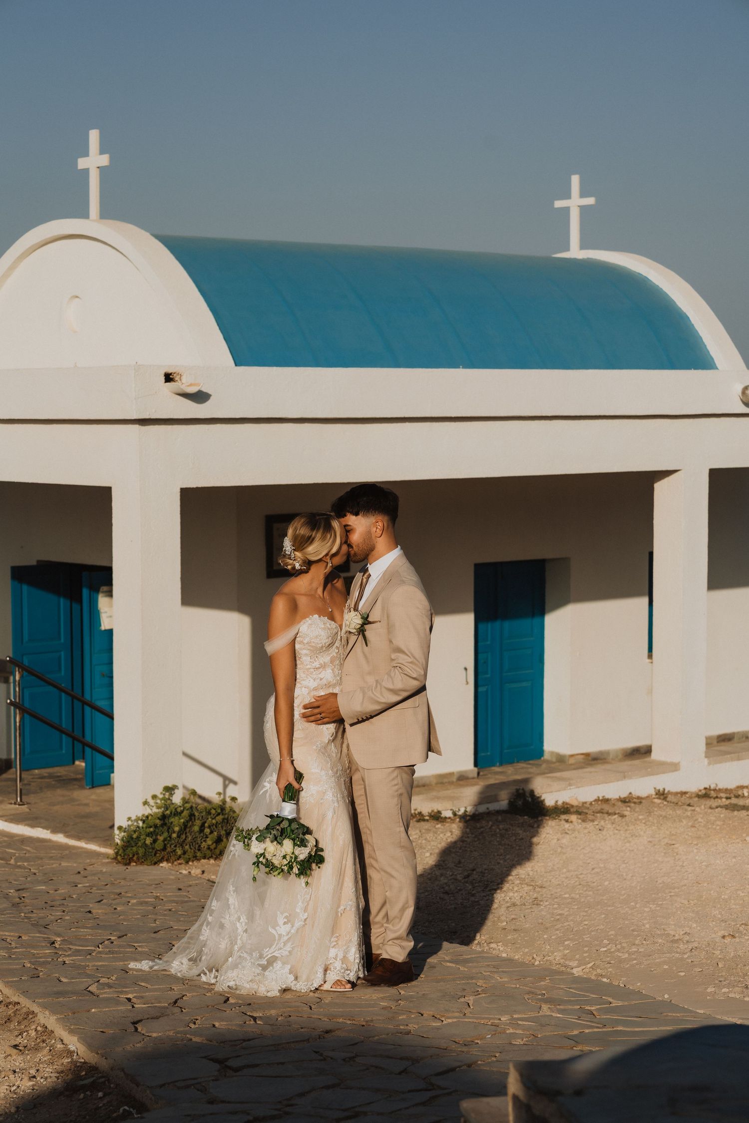 Intimate wedding moment captured outside a traditional Greek chapel with ocean views.