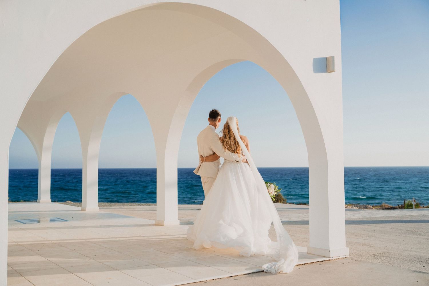 White arched Mediterranean architecture frames an oceanfront wedding scene.
