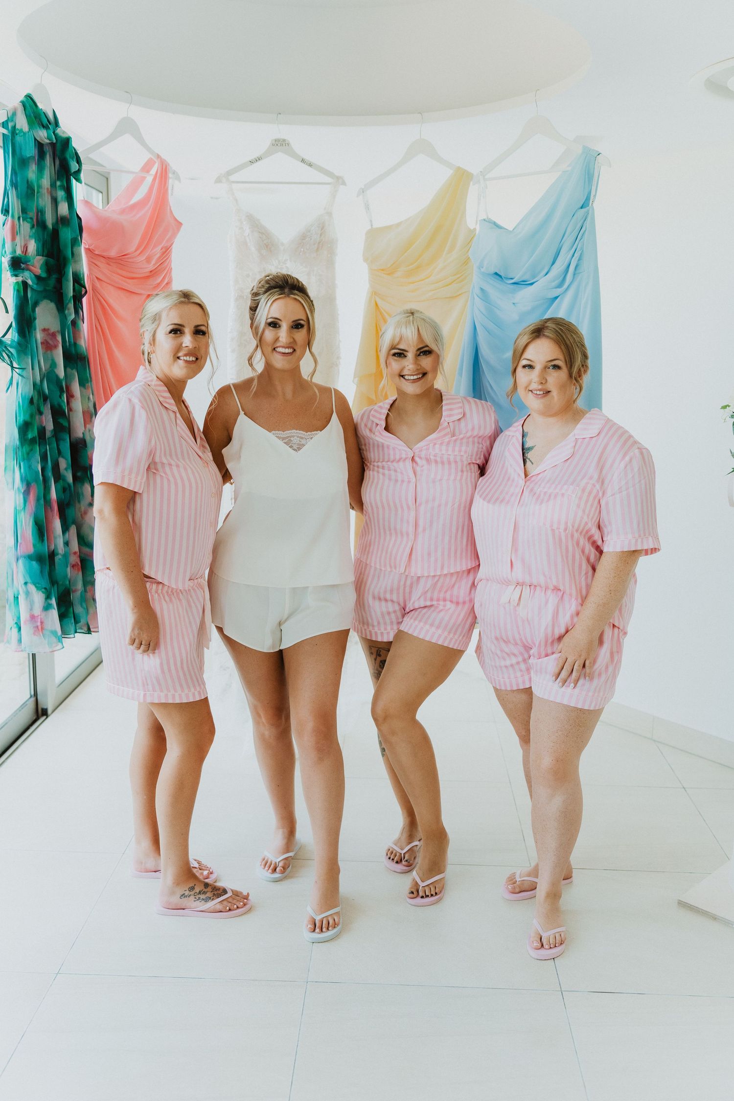 Group wearing matching pink striped pajama sets and white sandals pose together in a bright room with colorful fabrics.