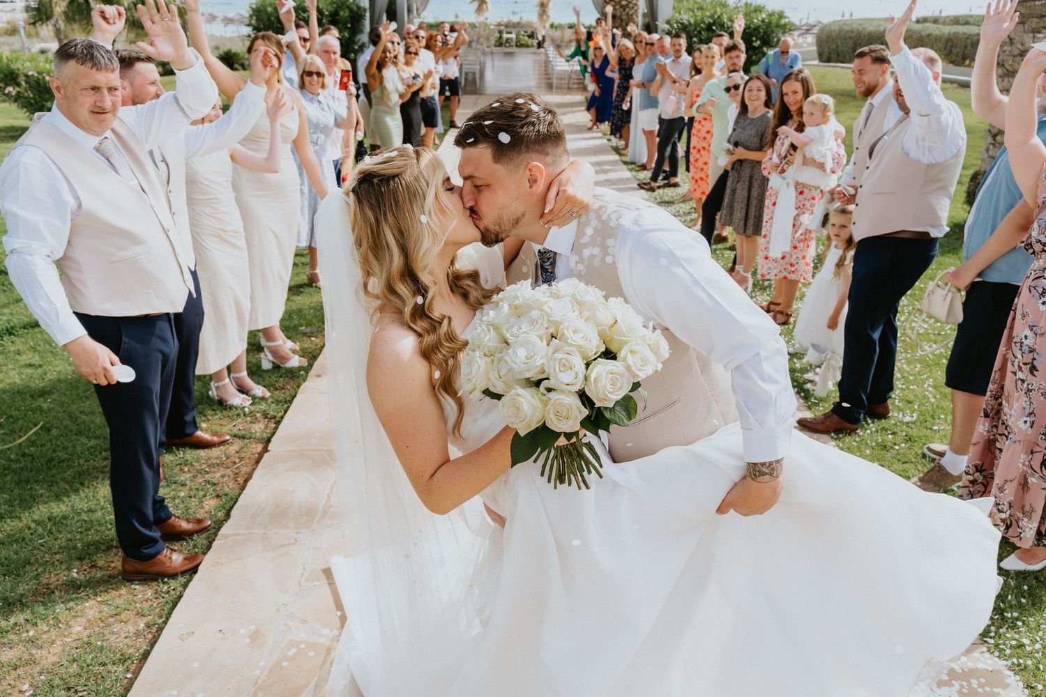 Wedding couple share a romantic kiss while guests create a pathway outside.