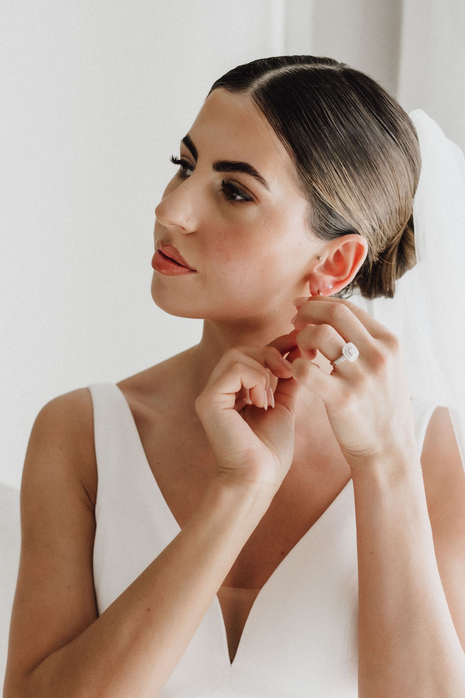 Close up of a bride wearing a white dress adjusting her earrings with sleek dark hair.