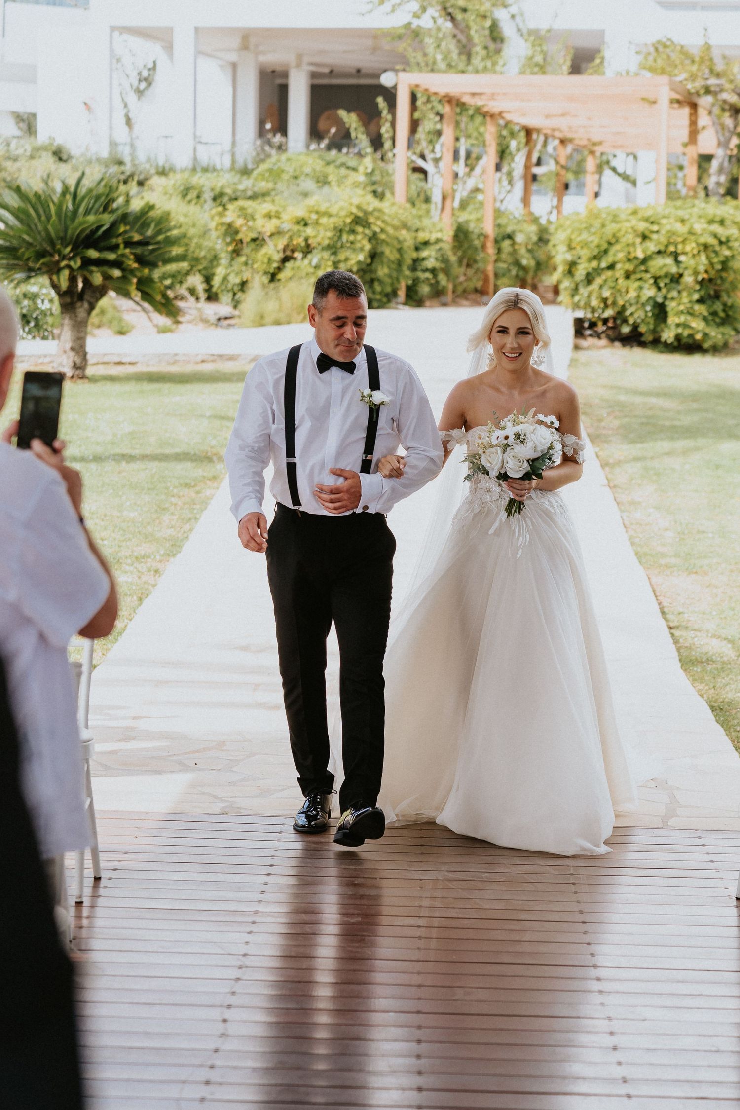 Wedding processional on a covered walkway surrounded by lush tropical landscaping.