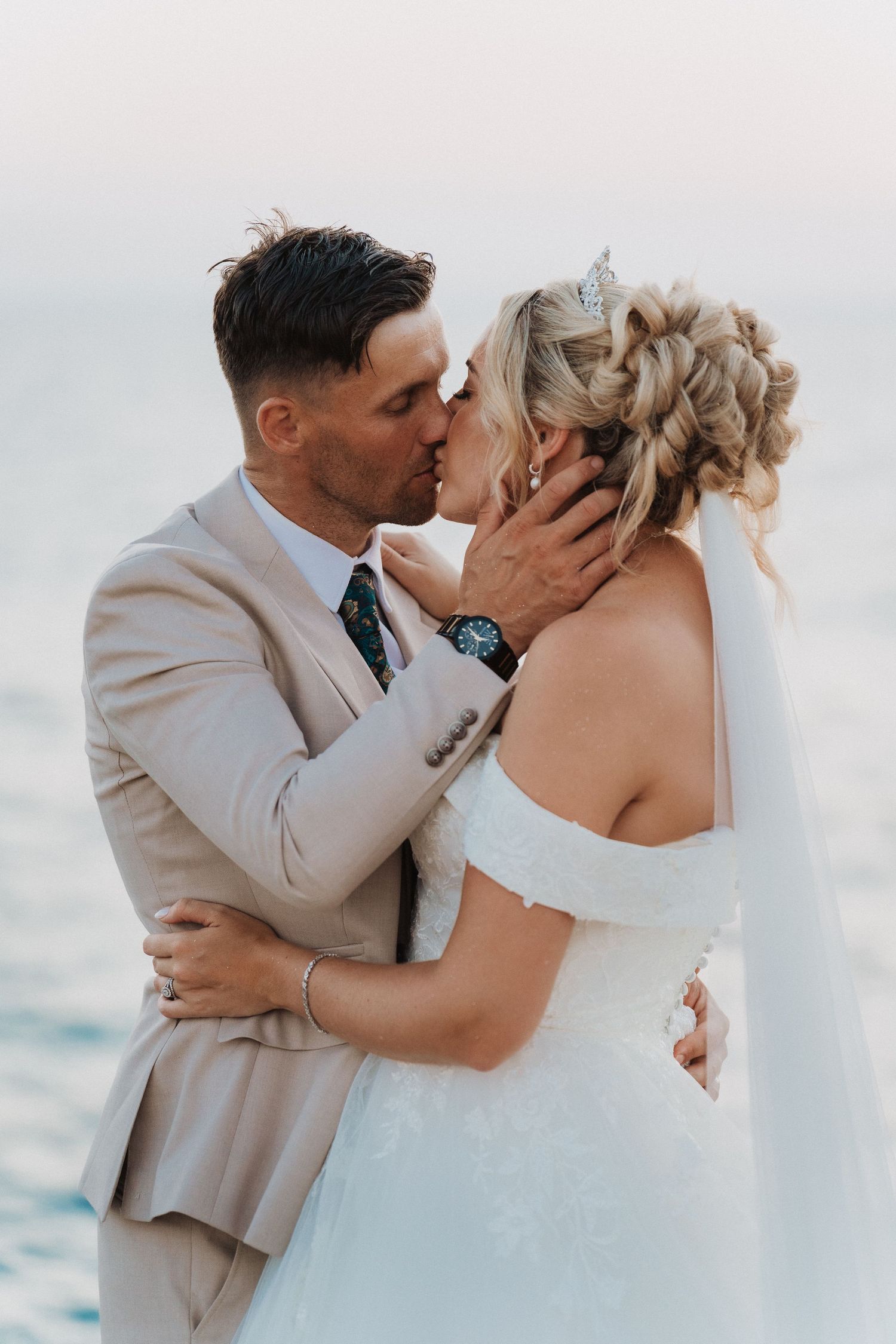Romantic wedding couple shares a kiss against an ocean backdrop during sunset.