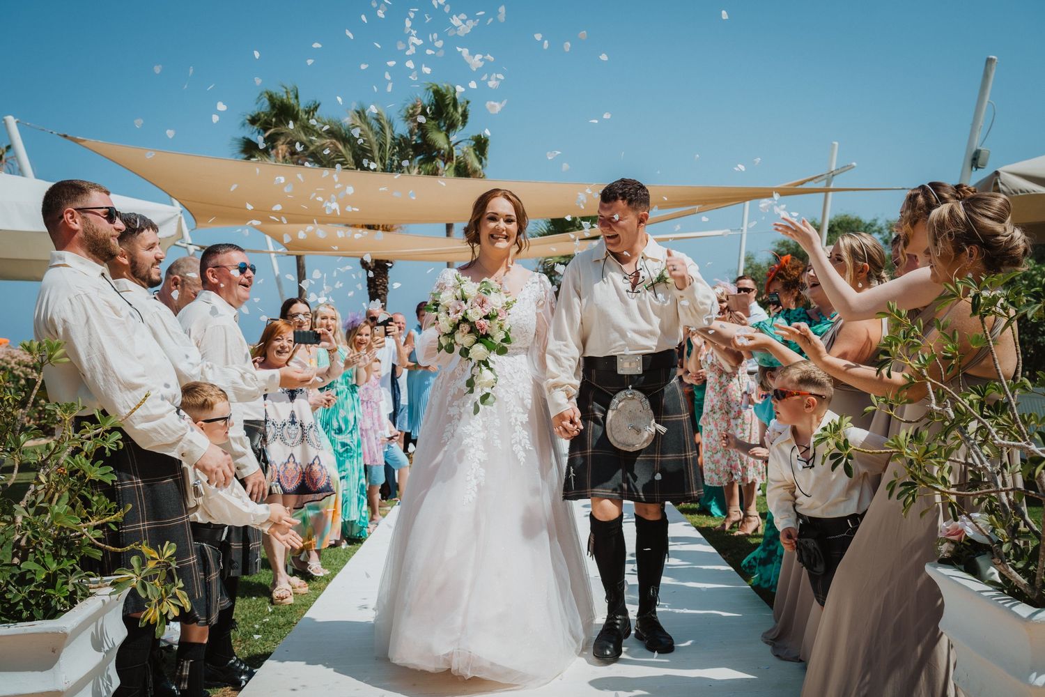 Wedding celebration with confetti being thrown at couple on white aisle runner outdoors.