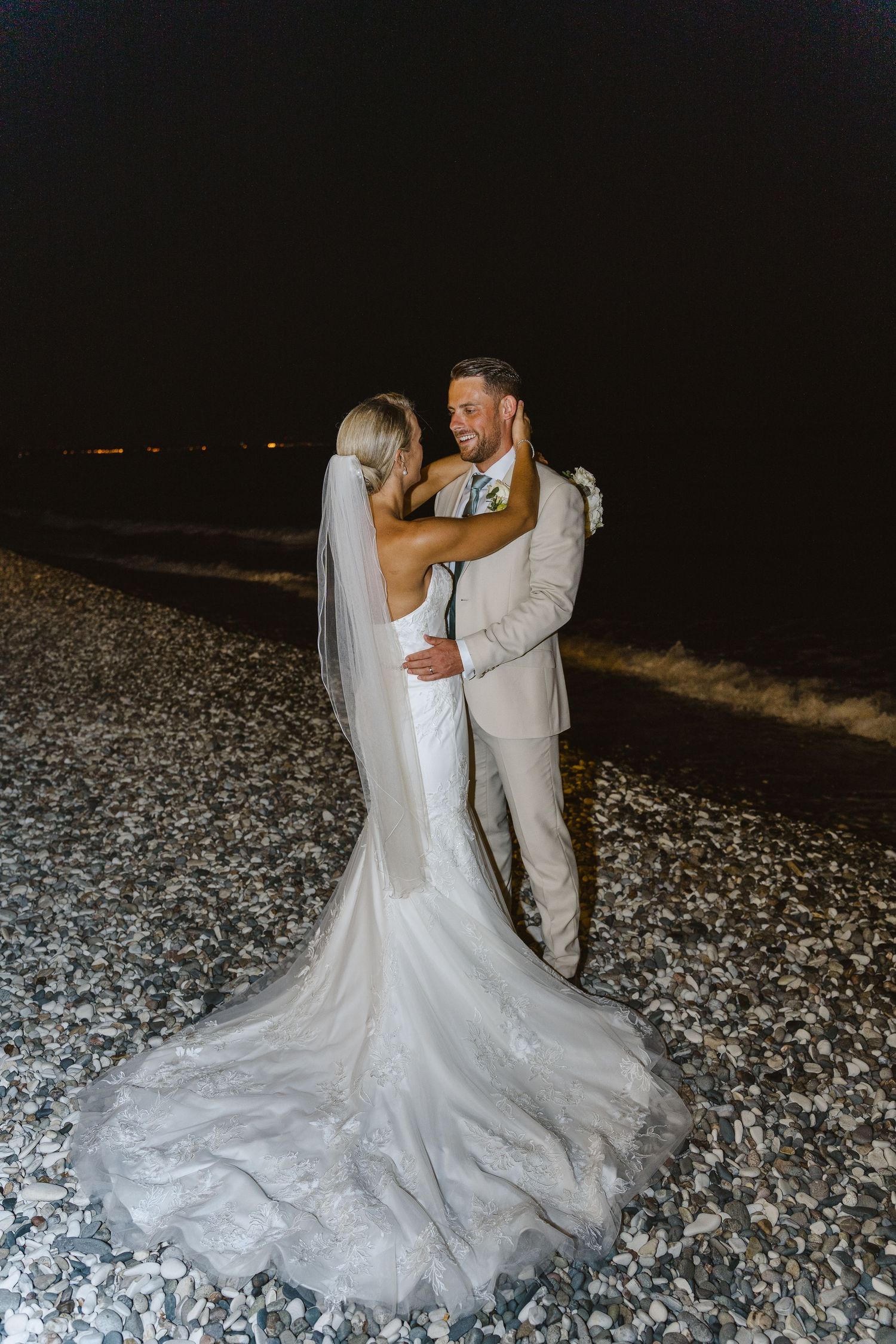 Beautiful wedding gown with lace train cascades over rocky beach during evening portraits.