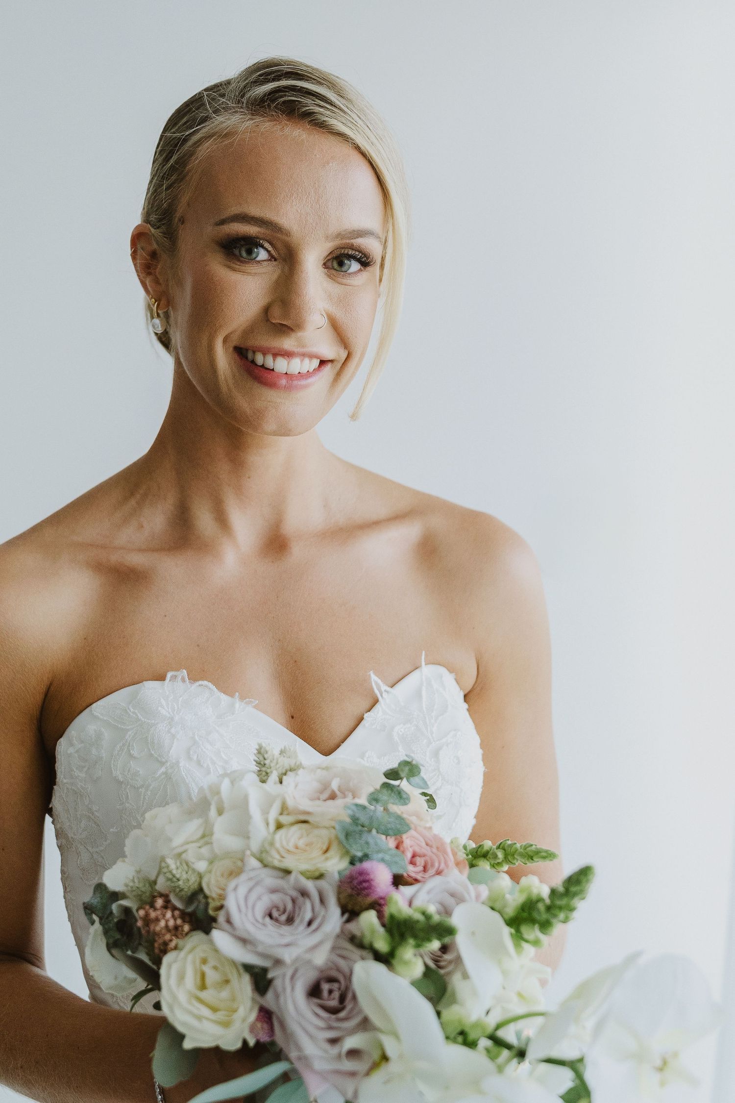A bride in a white strapless wedding dress holds a beautiful bouquet of white and blush pink roses and flowers.