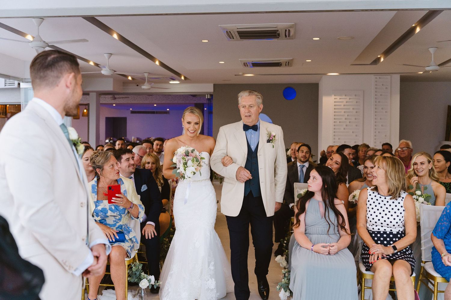 Wedding ceremony in a modern indoor venue with a well-dressed couple and guests gathered in formal attire.