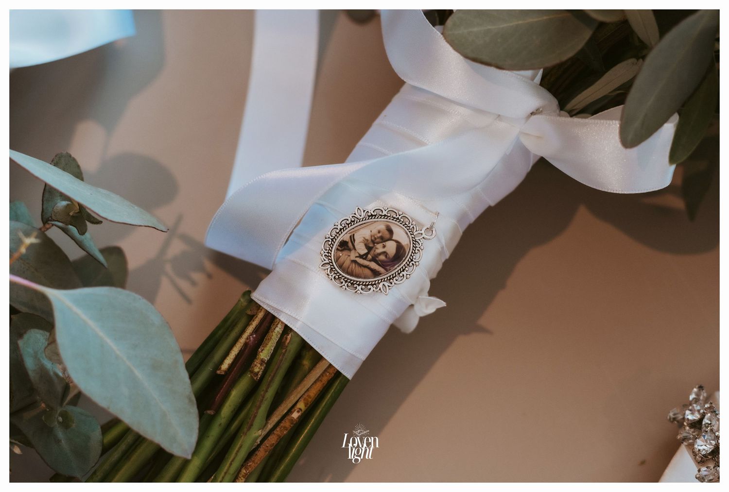 Wedding bouquet wrapped in white ribbon with decorative medallion detail.