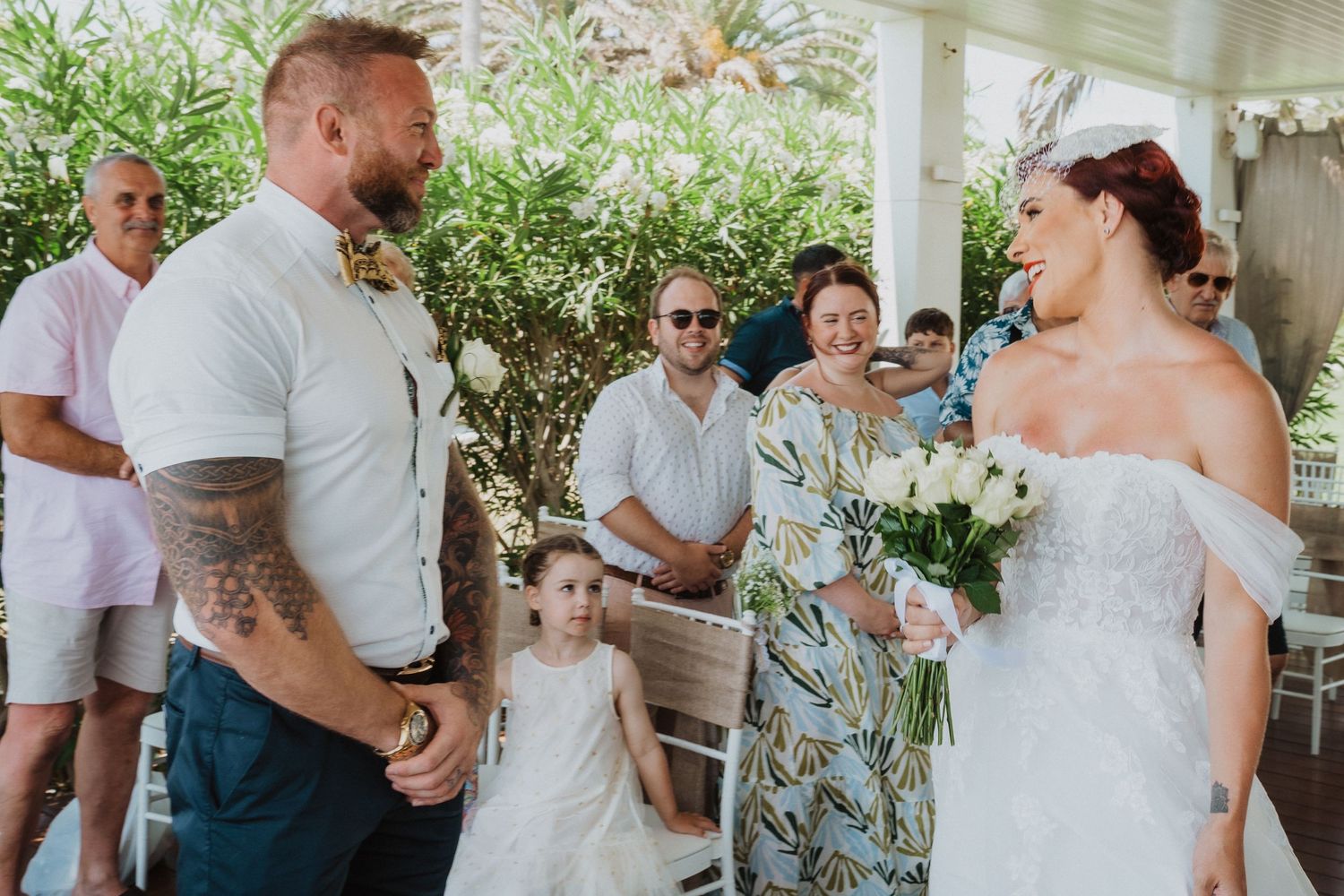 Wedding guests and couple gather under a white covered porch during an intimate ceremony.