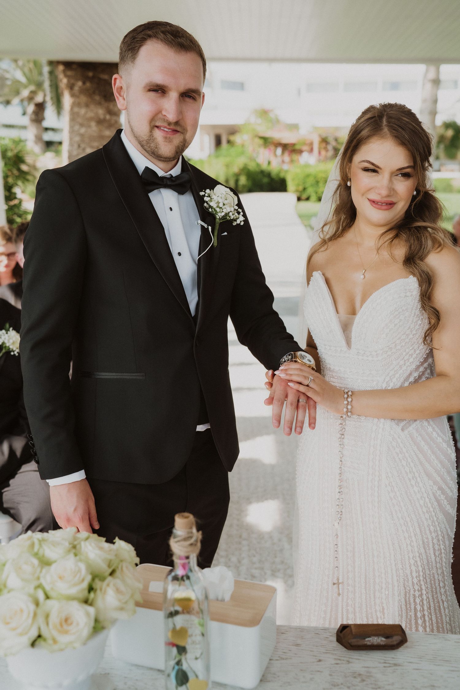Bride and groom smiling together at wedding altar with white roses and ceremony accessories.