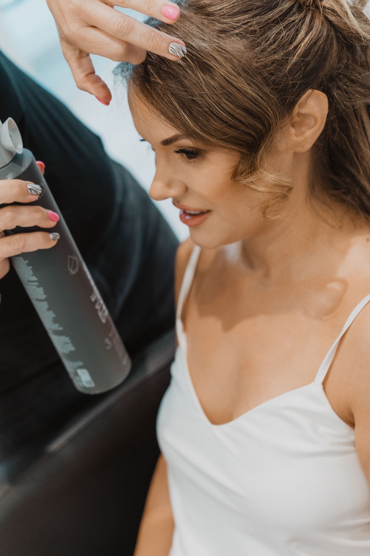 Hairstylist applying hairspray to brunette bride during wedding day preparations.