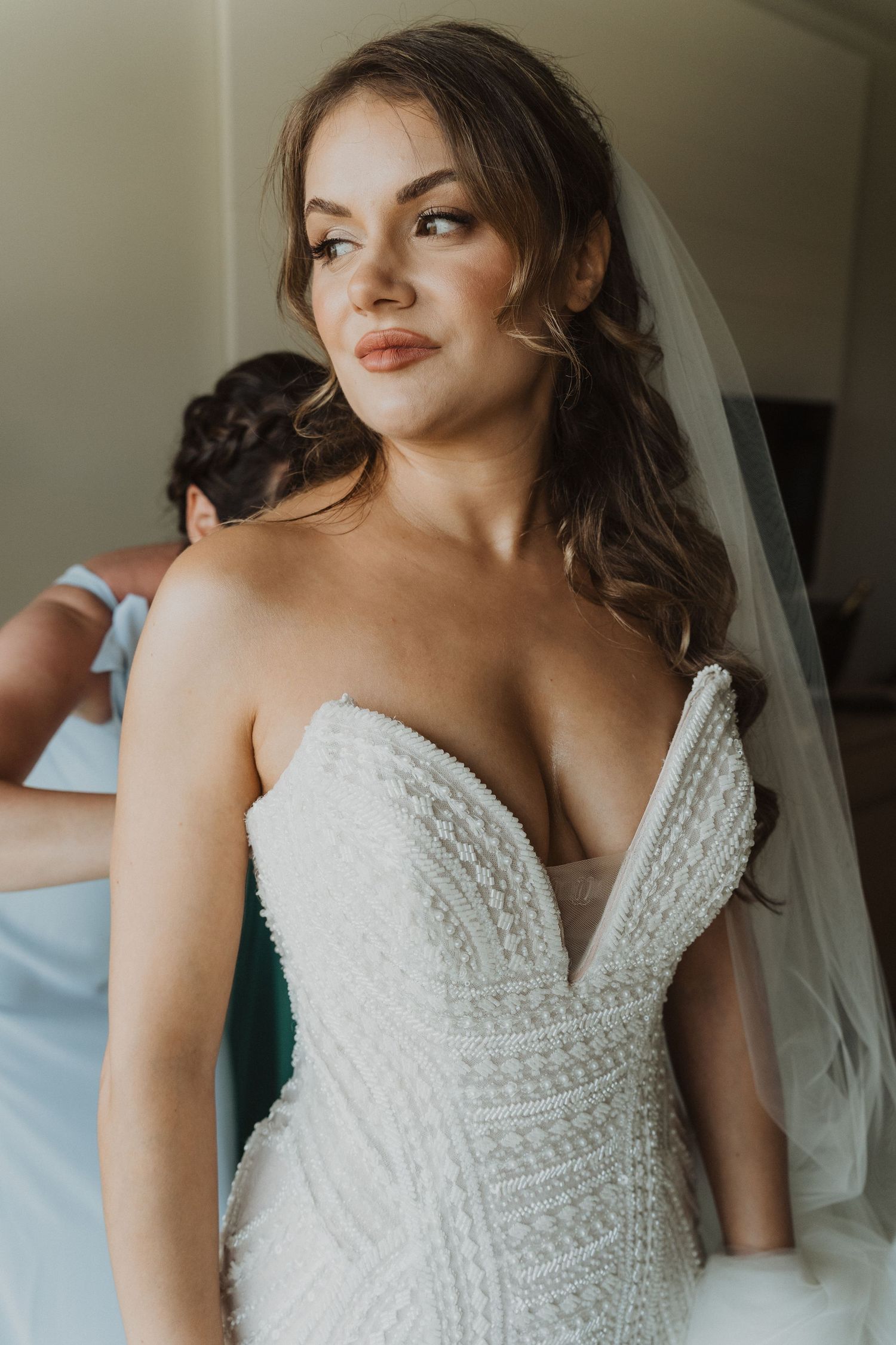 Beautiful bride in strapless beaded wedding gown being helped into dress by bridesmaid.