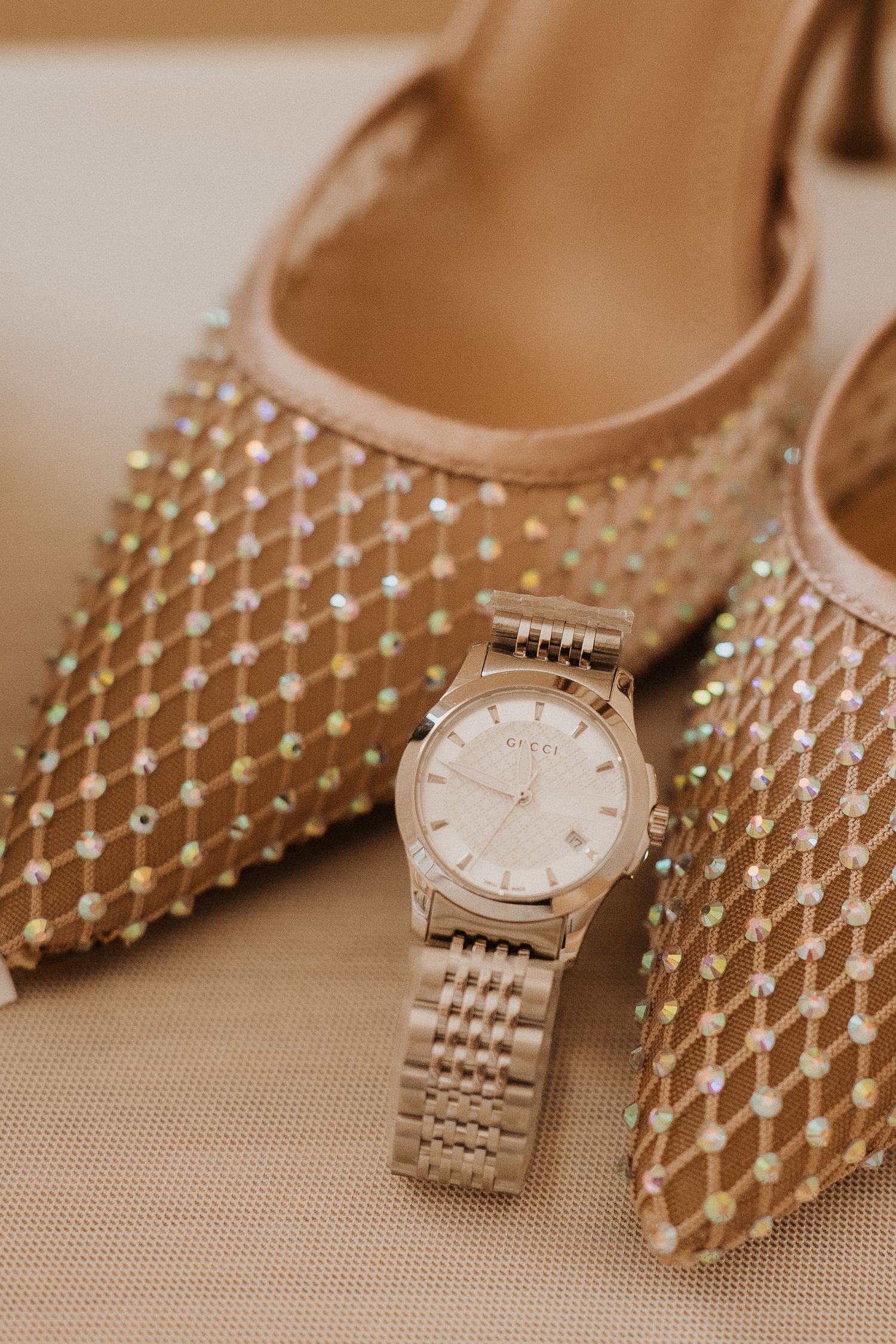 Elegant gold studded pointed toe heels paired with a classic metallic watch on beige background.