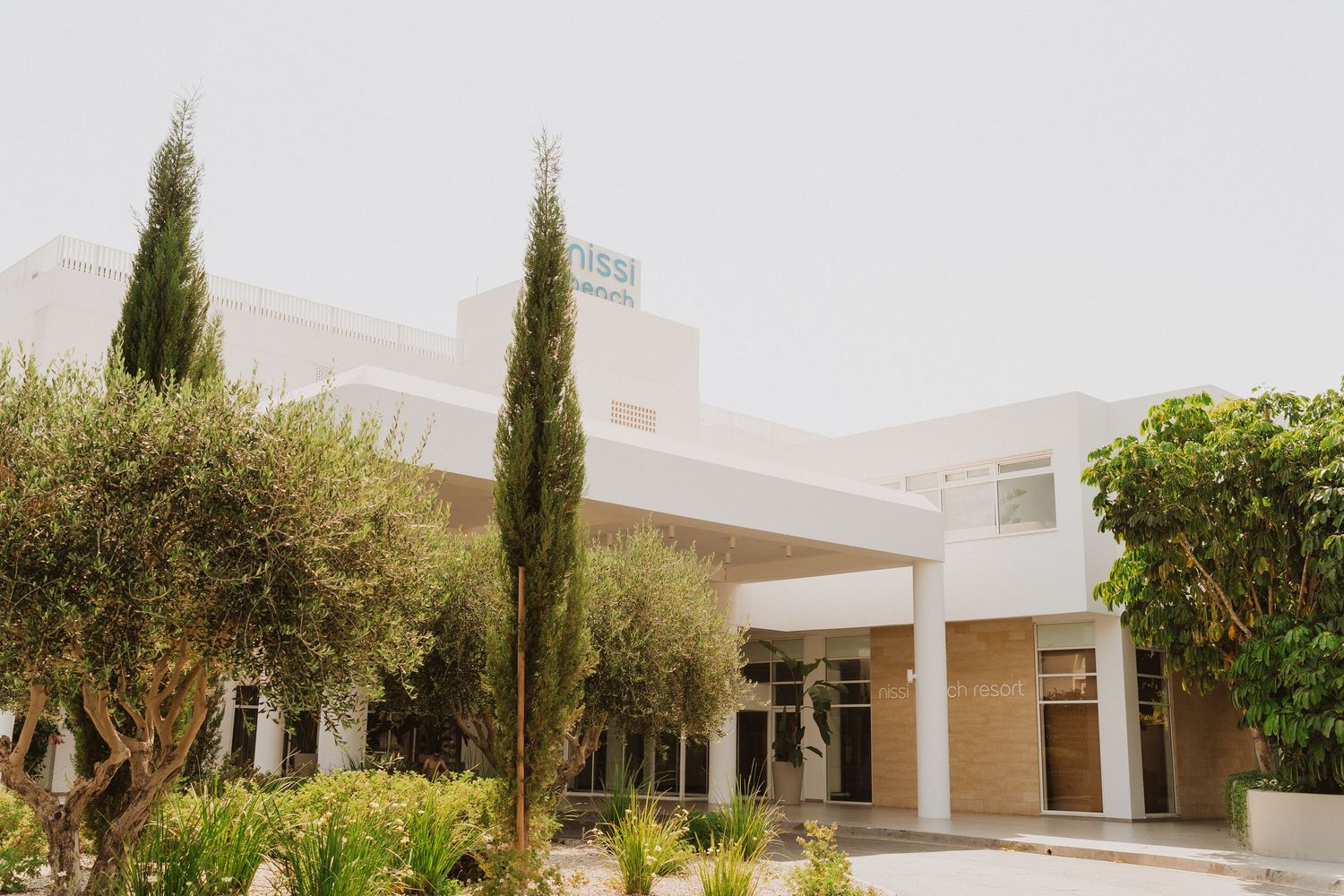 Modern white commercial building exterior with tall cypress trees and landscaping in a Mediterranean style setting.
