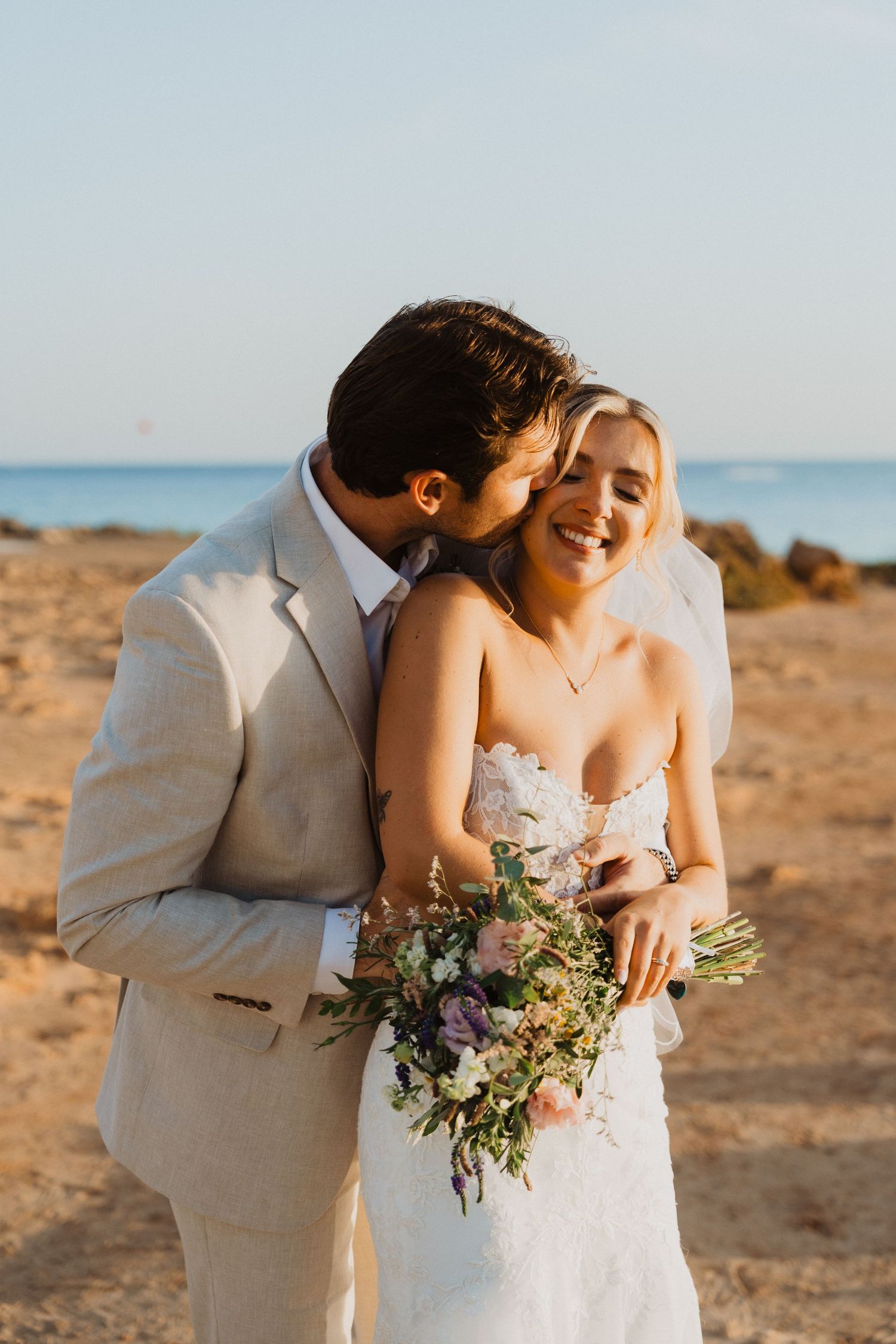 Sunset beach wedding photos capture tender moments between newlyweds with ocean view.