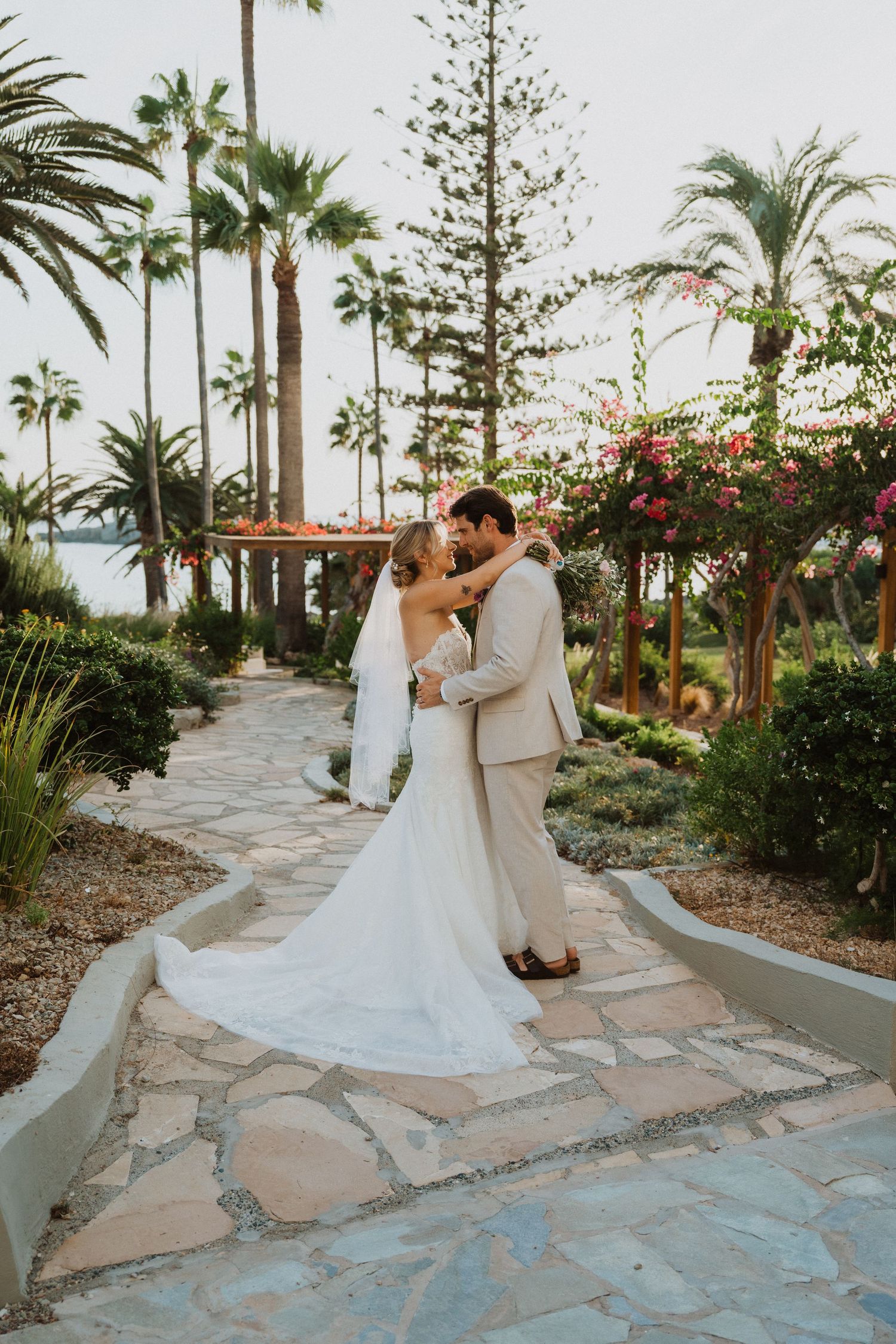 A romantic wedding photoshoot on a curved stone pathway with palm trees and ocean views.