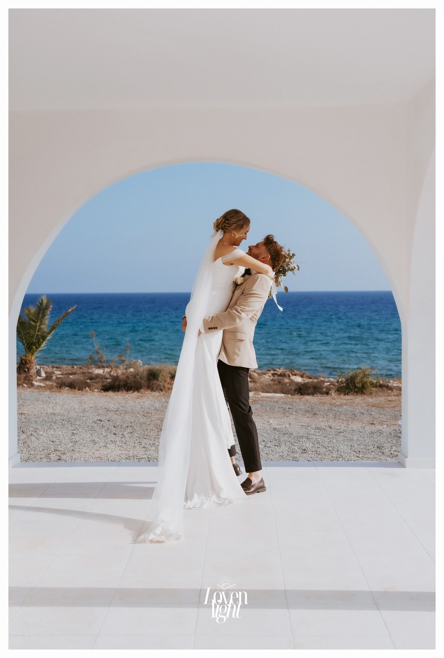 Romantic couple embrace under a white archway overlooking the Mediterranean Sea.