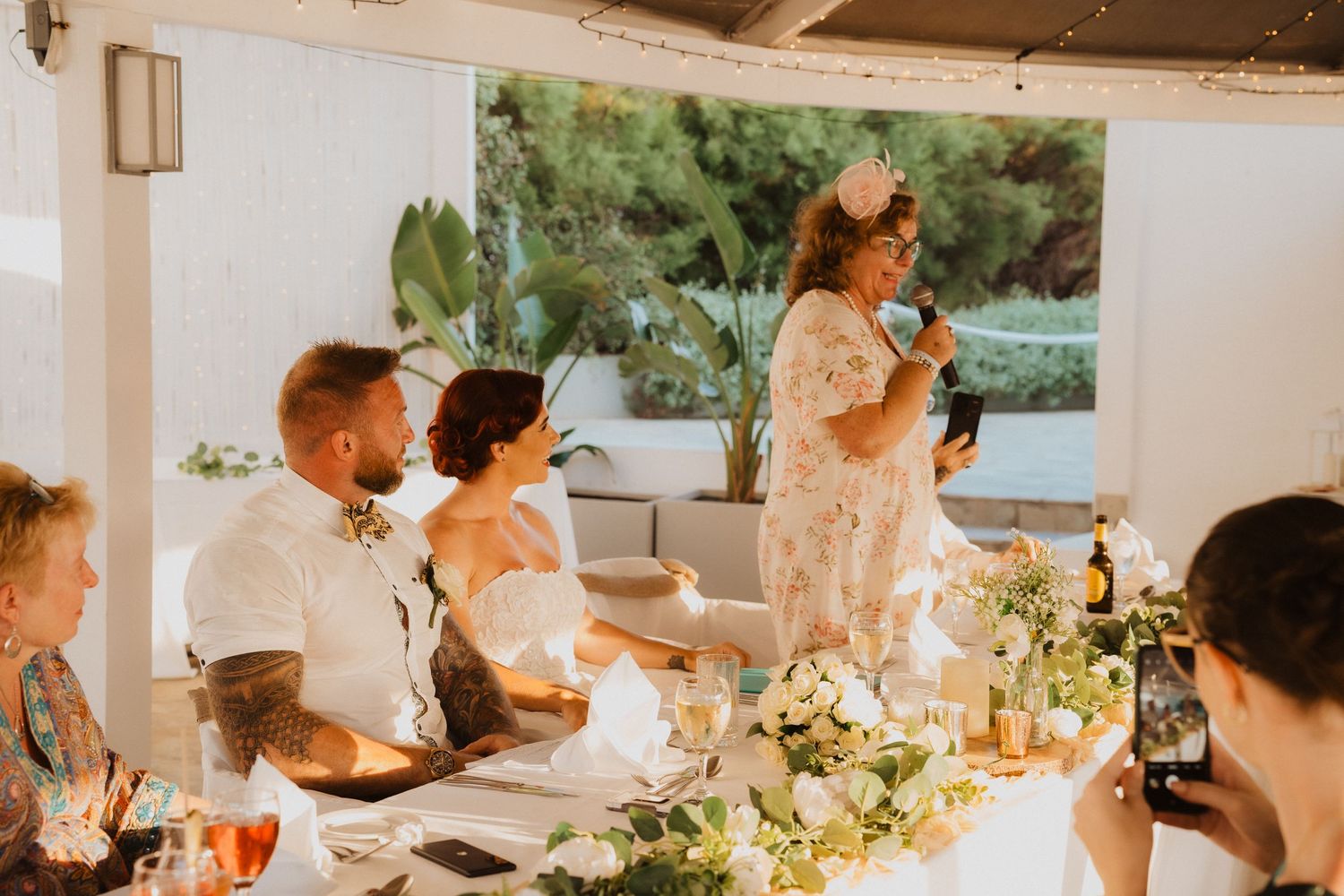 Wedding celebration dinner with guests seated at elegantly decorated table with floral centerpieces.