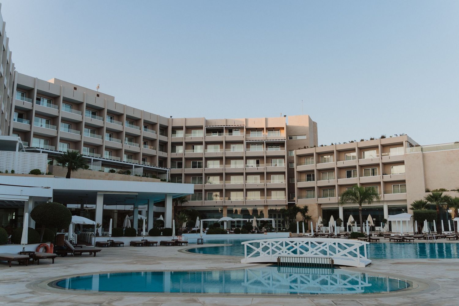 Modern beachfront hotel with multiple floors and a large swimming pool in the foreground.