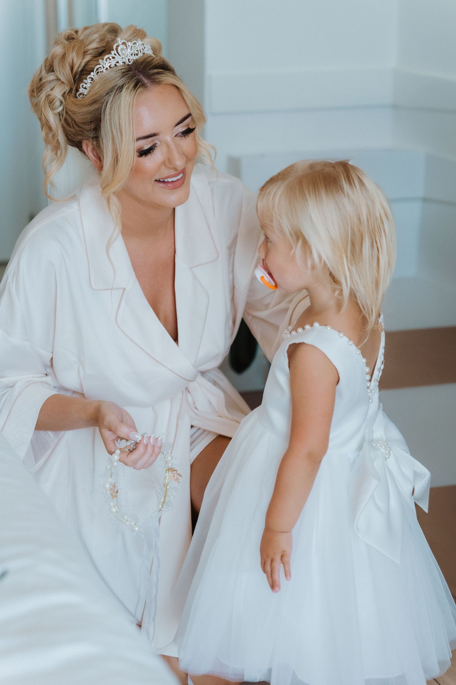 A tender moment shared between a little girl in a white tulle dress and someone in a white robe with a tiara.