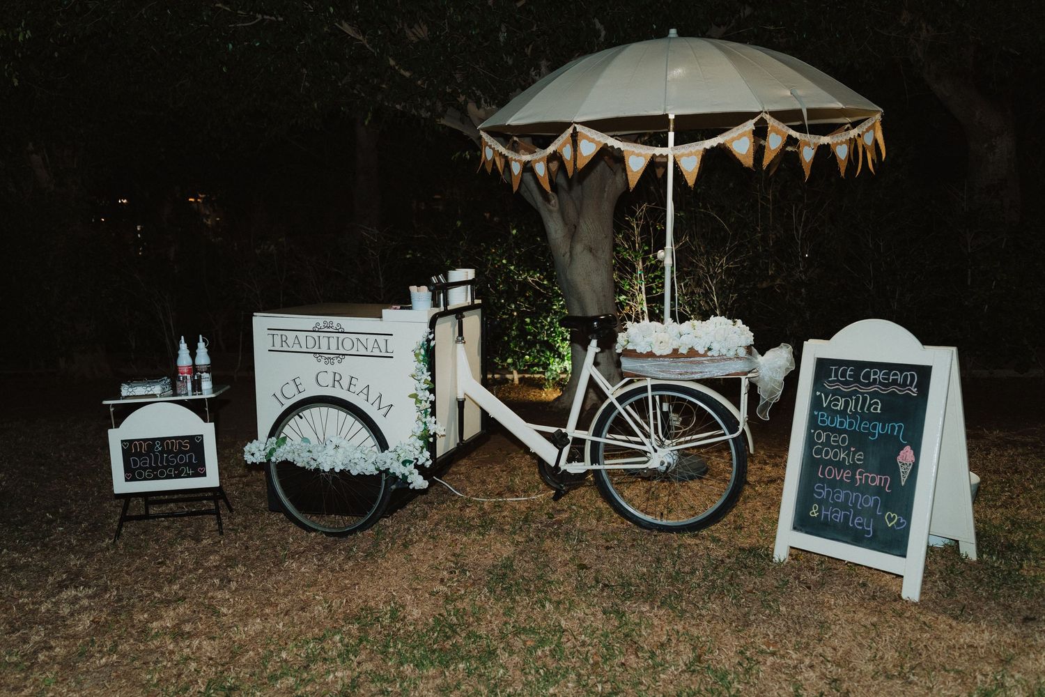 Vintage white bicycle with umbrella and chalkboard signs set up as a charming wedding drinks station.