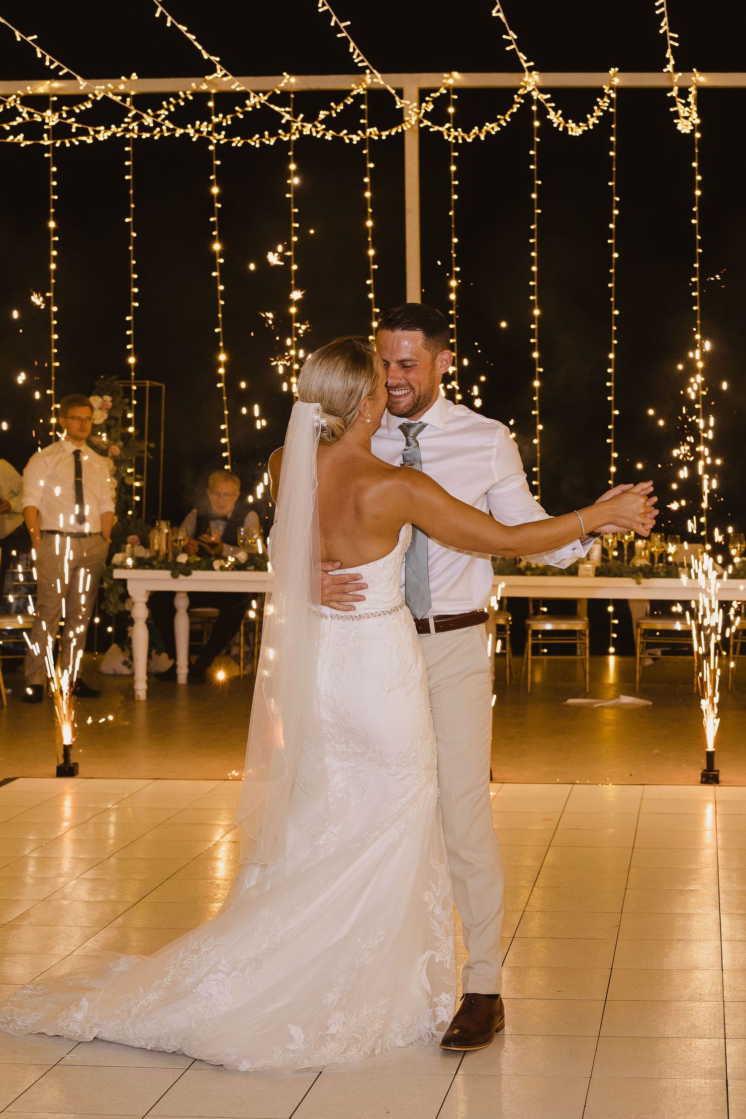 A couple dances beneath cascading fairy lights with sparklers adding magical ambiance.