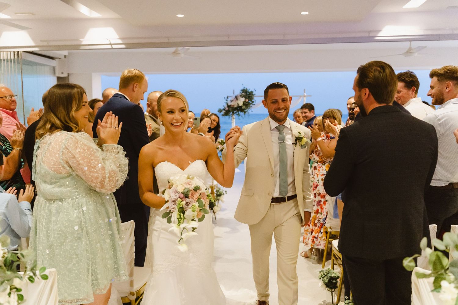 Newlyweds celebrate while walking down flower-decorated aisle with guests cheering.