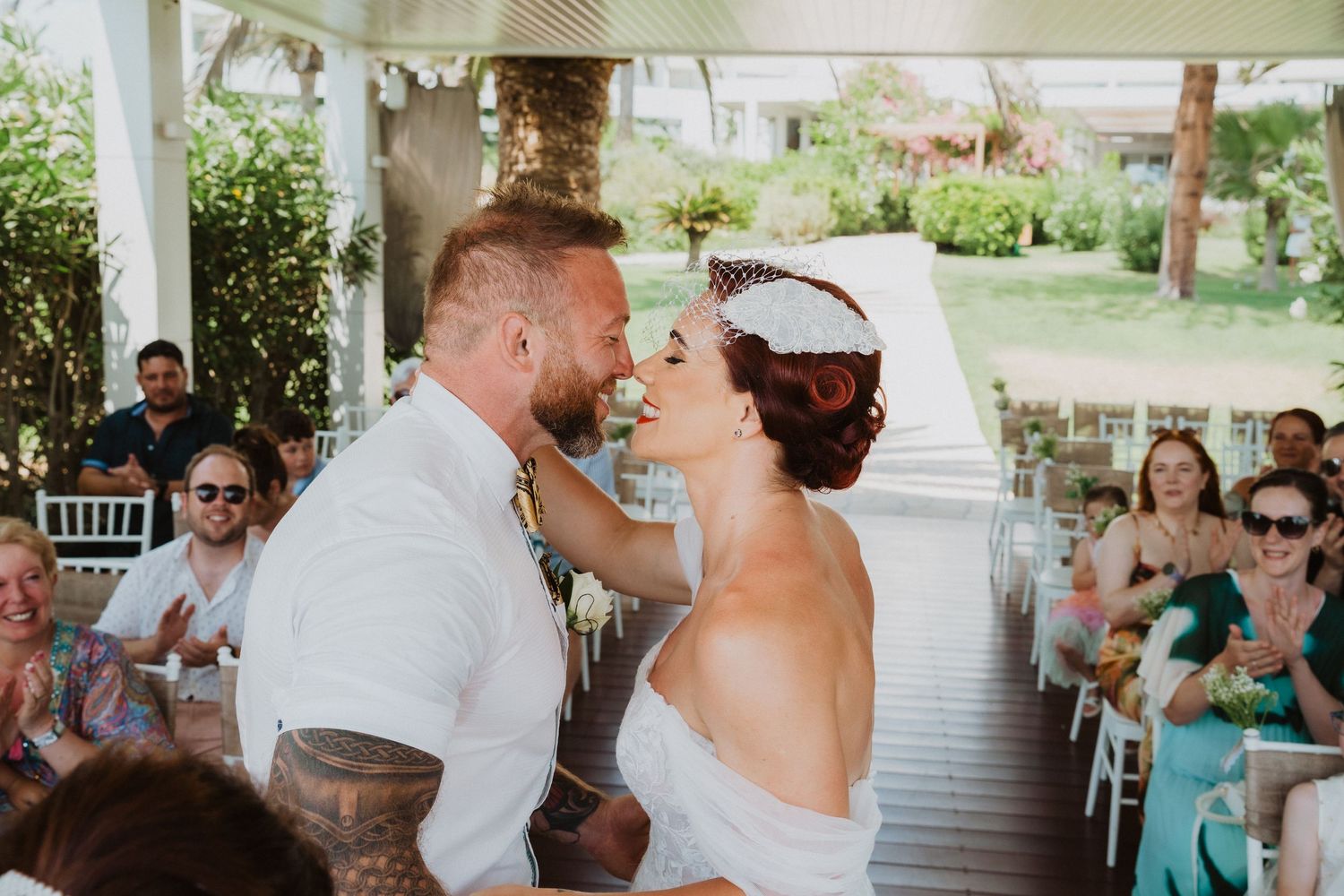 A romantic wedding ceremony taking place under a covered outdoor venue with guests watching.