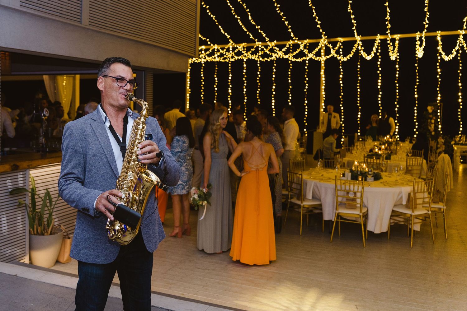 Professional saxophone player performs at an elegant wedding reception under golden string lights.