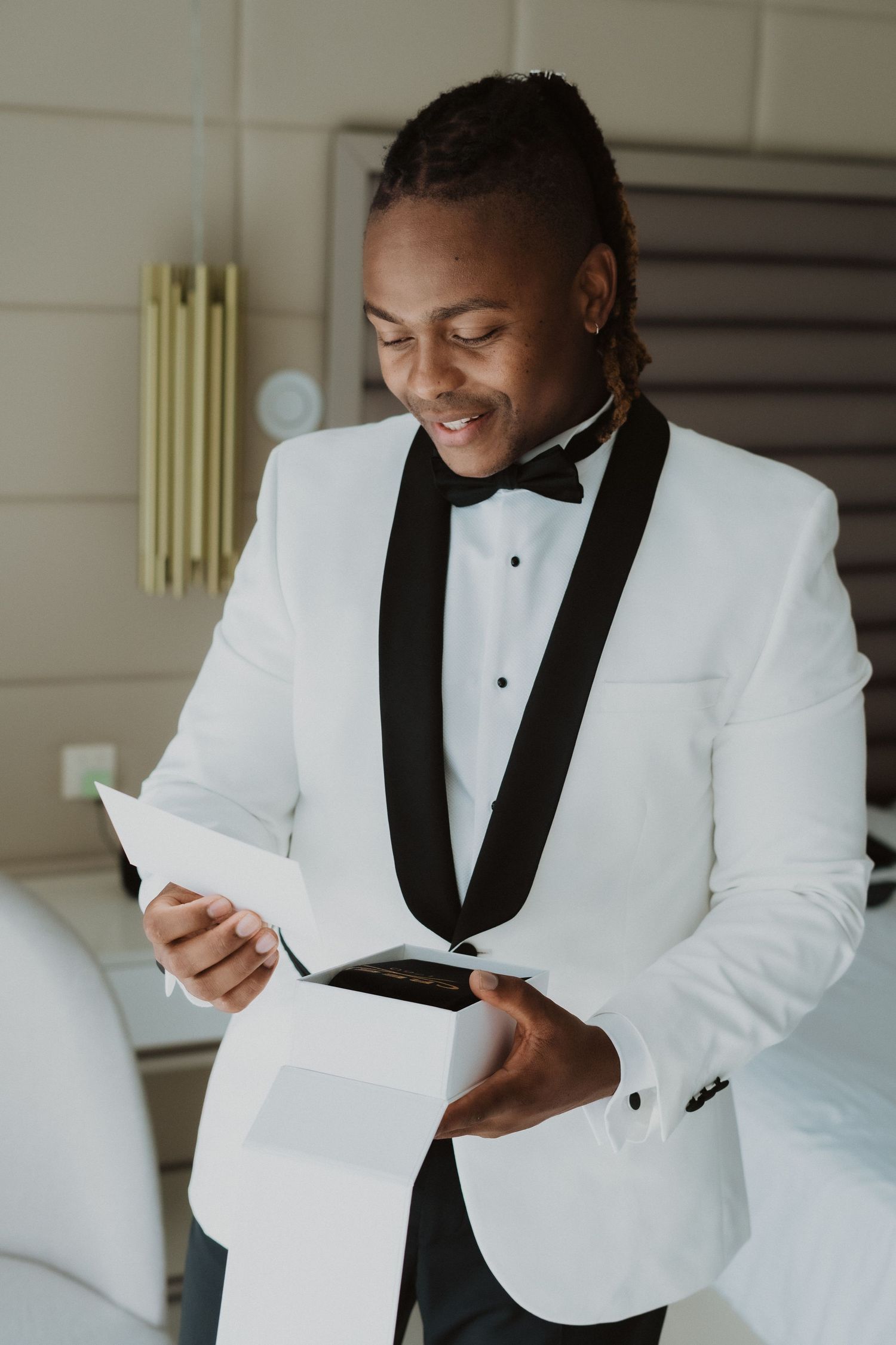 A person in a white dinner jacket smiles while reading a document.
