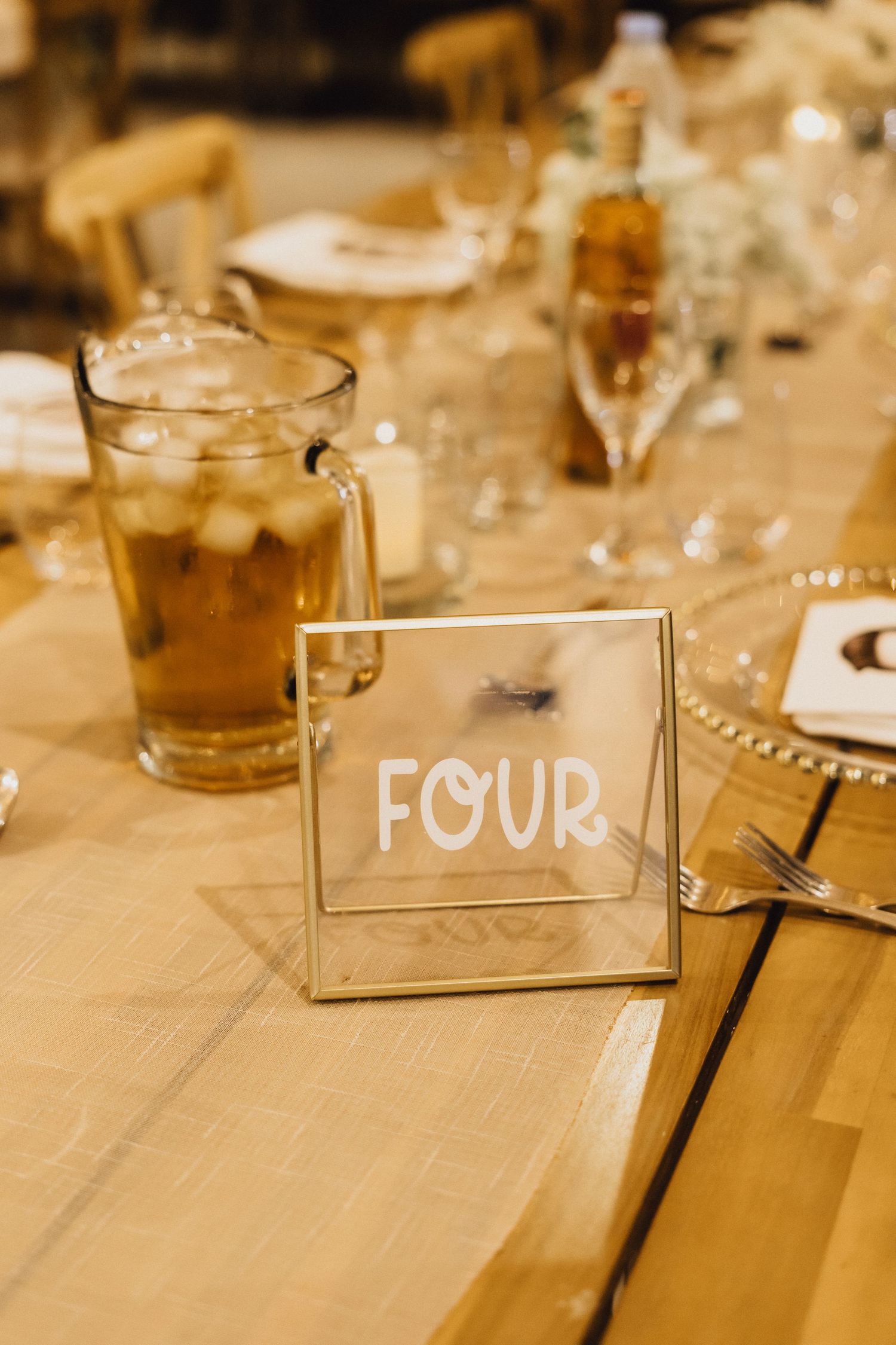 Table number 'FOUR' displayed in gold frame with beverages and place settings.