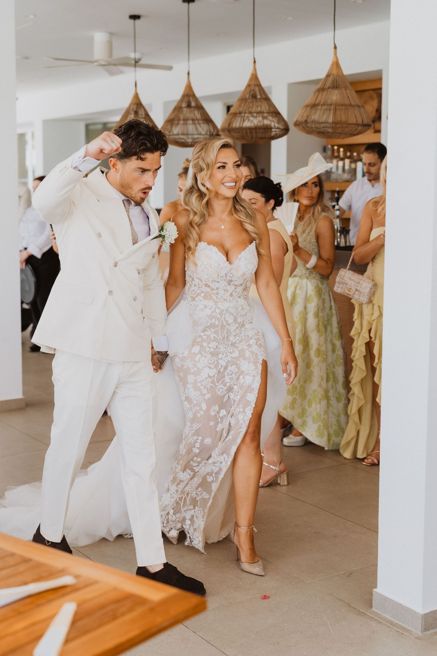 Couple in elegant white attire dancing at a wedding reception under woven pendant lights.