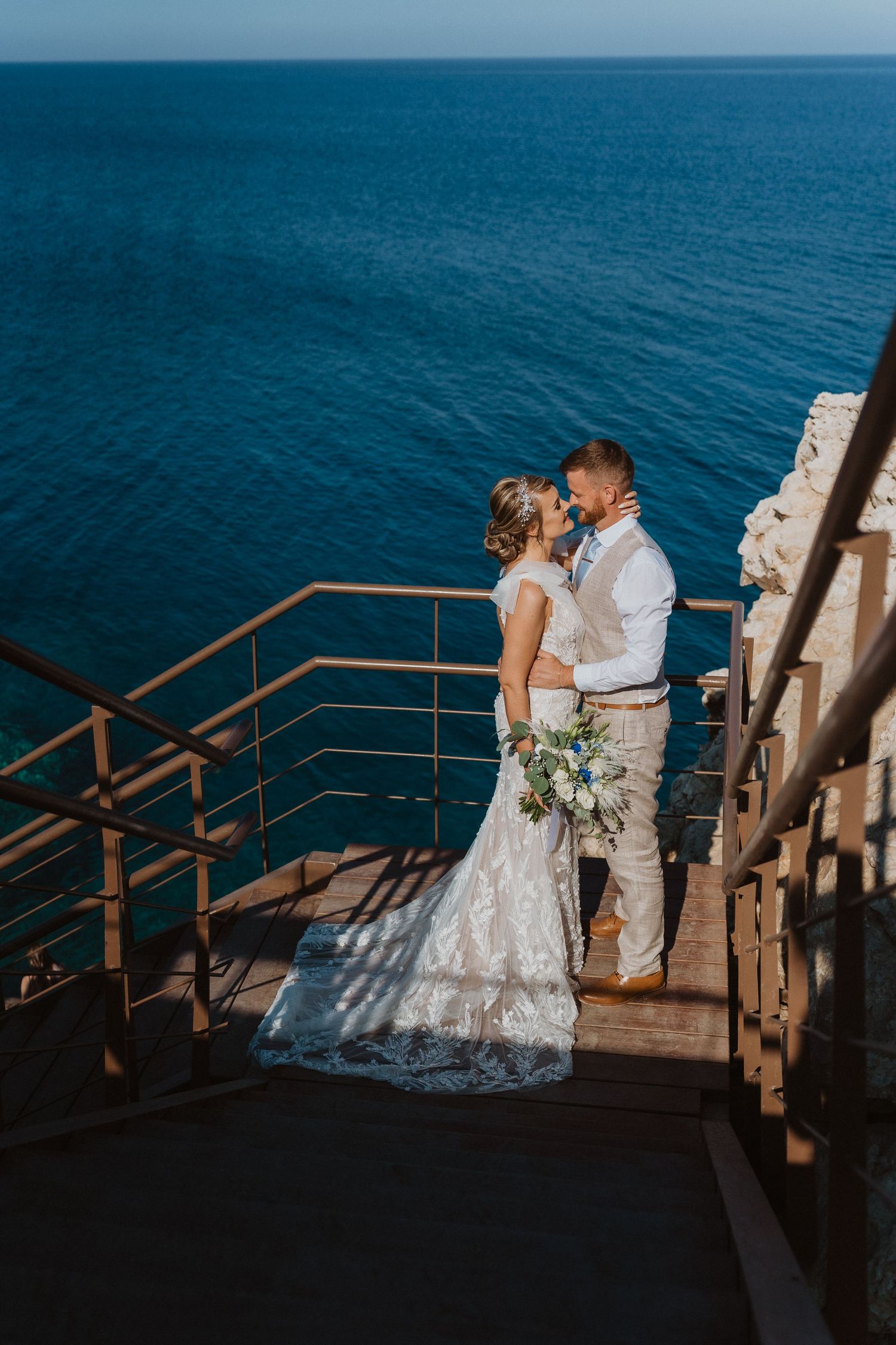 Wedding couple standing on wooden stairs against dramatic ocean backdrop.