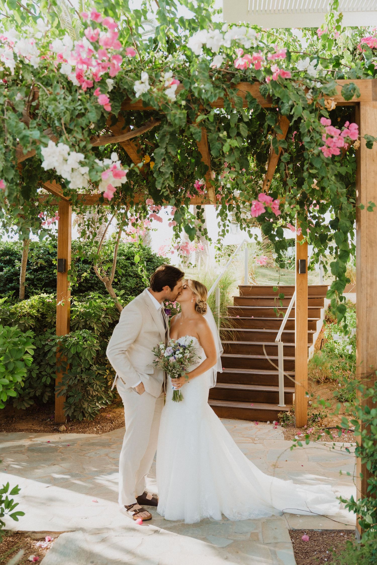 Romantic wedding photos under pergola with pink bougainvillea flowers and greenery.