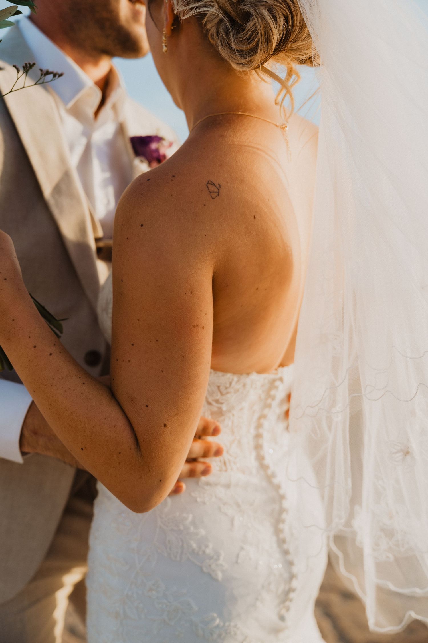 Close-up details of lace wedding dress and intimate moment between newlyweds.