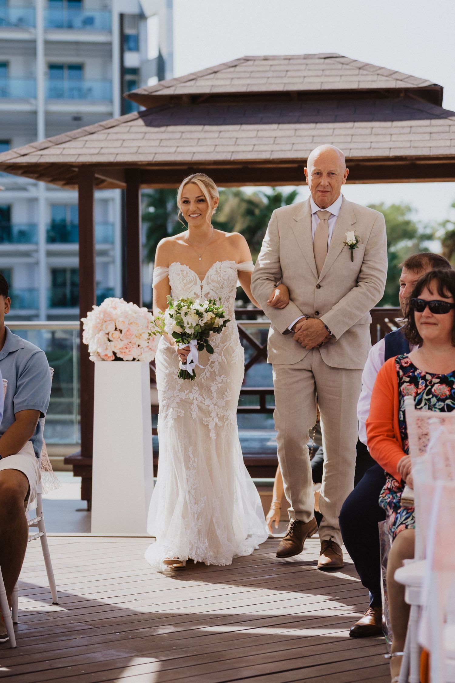 Outdoor wedding ceremony with white columns and covered pavilion on a wooden deck.