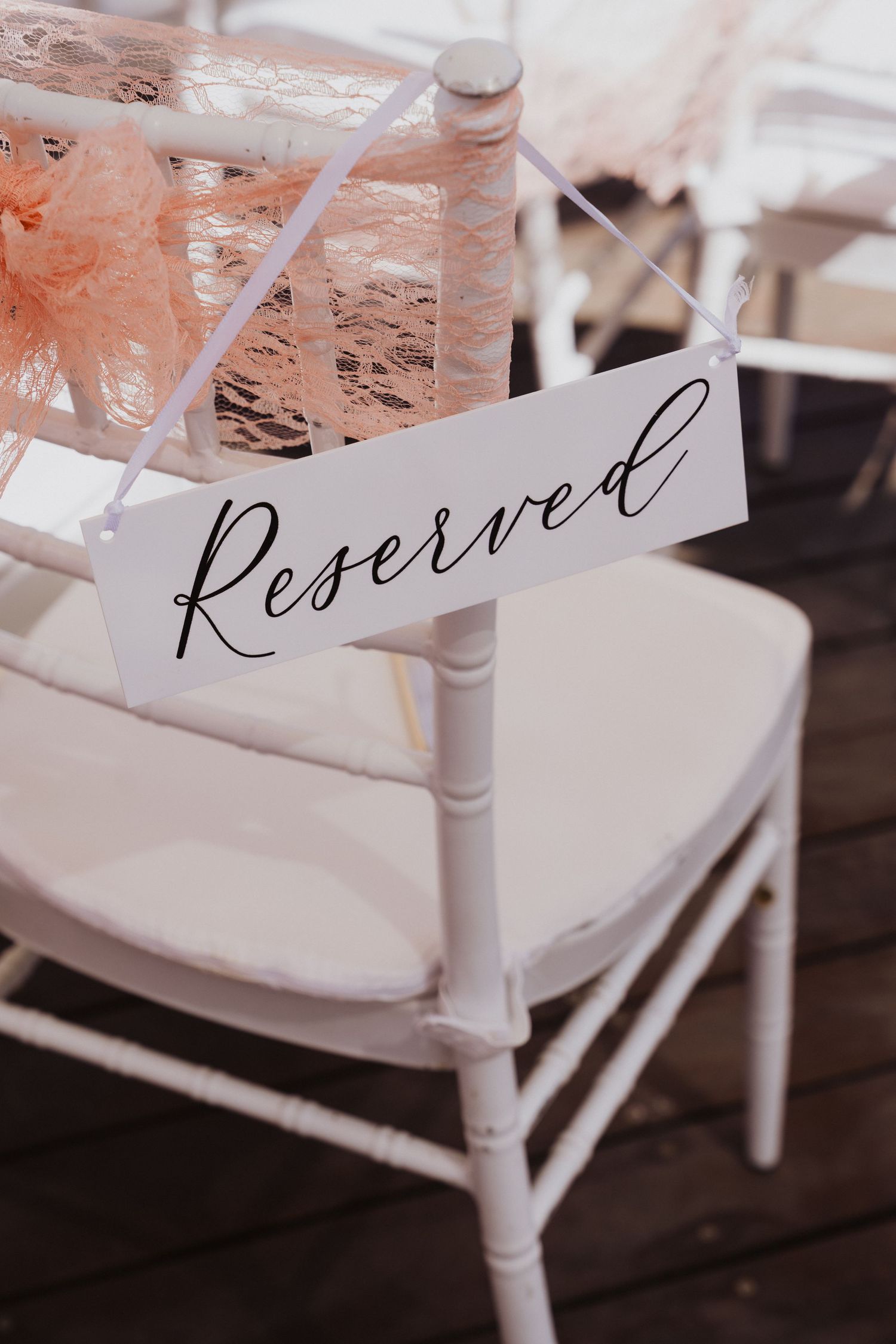 White wedding chair with reserved sign and peach lace decoration.