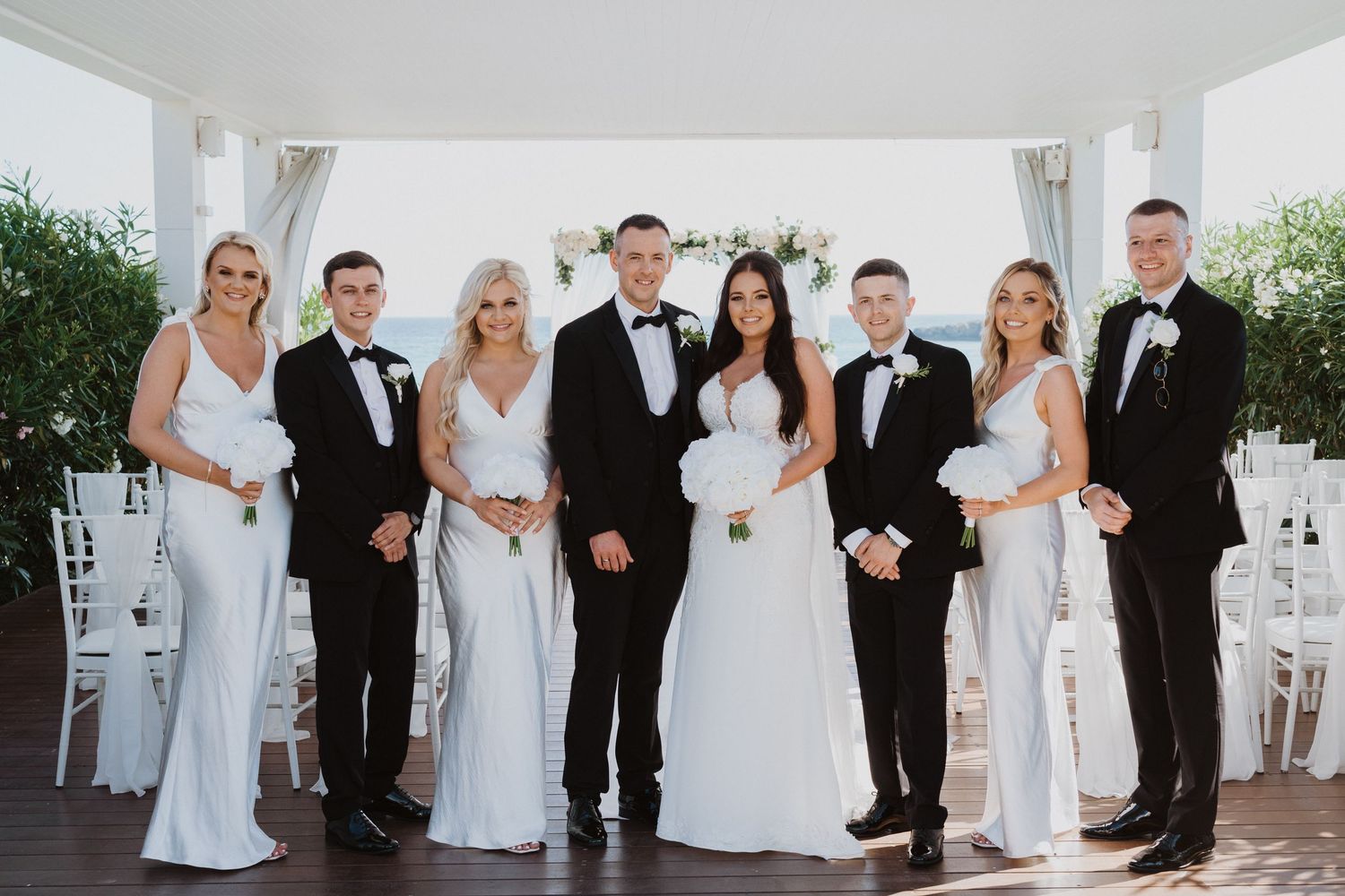 Wedding party members lined up in formal attire at a bright indoor venue.