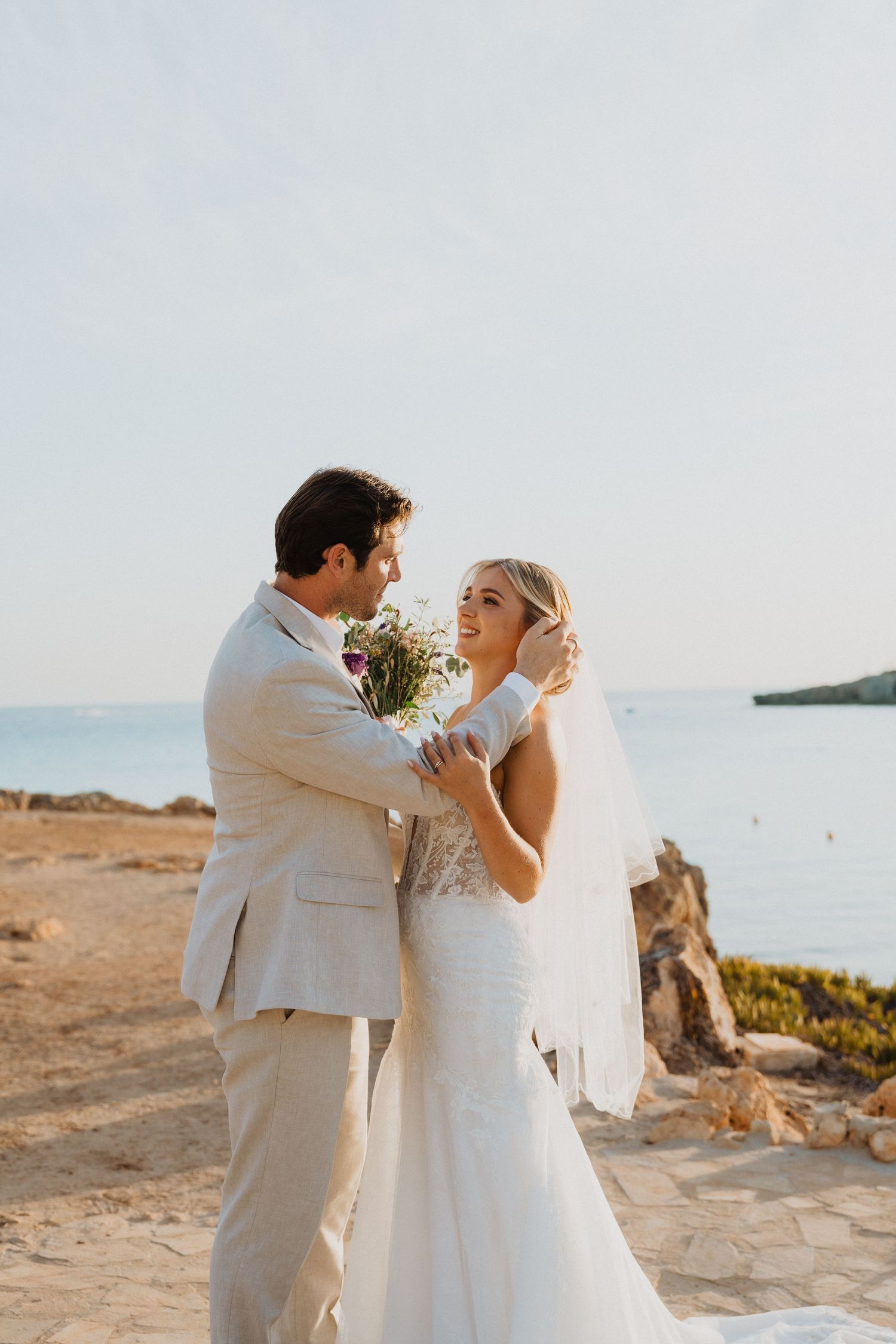 Romantic seaside wedding portrait with couple embracing against ocean backdrop.
