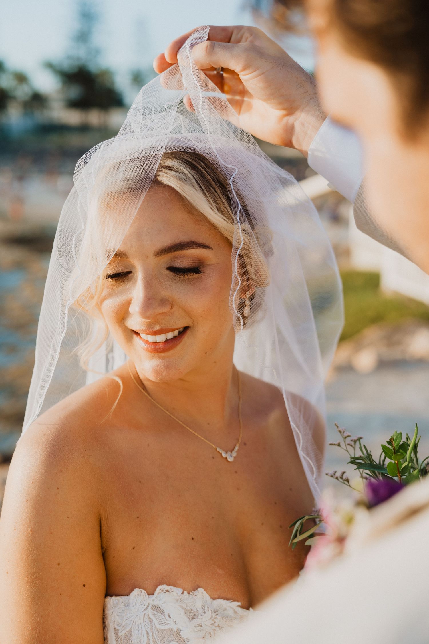 Close-up shots of bride smiling while veil is adjusted during outdoor wedding ceremony.