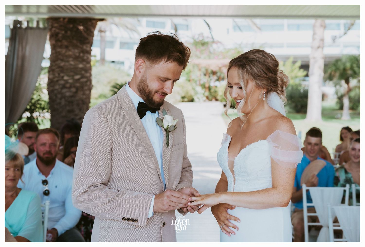 A couple exchanges rings during their garden wedding ceremony surrounded by guests.