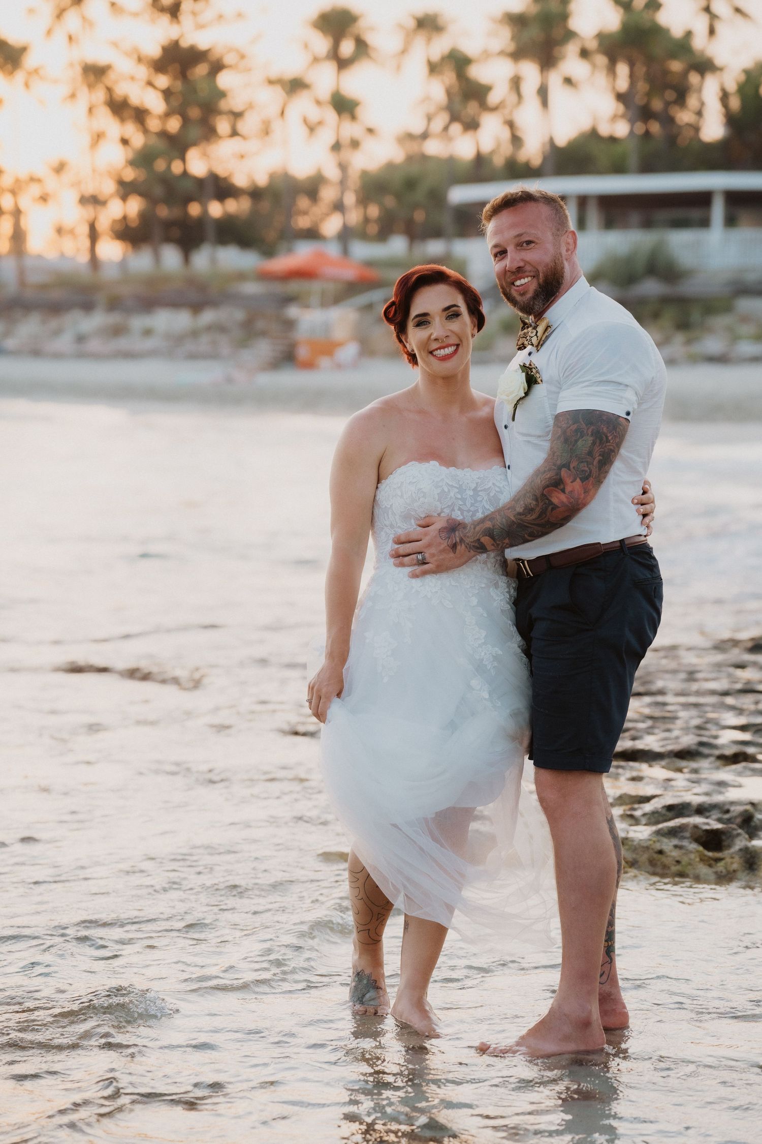 Beachside wedding portrait at sunset with couple standing in shallow water.