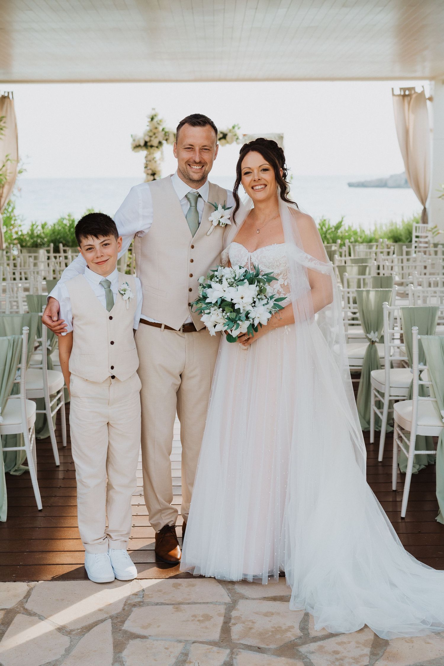 A wedding ceremony at a waterfront venue with white chairs and floral decorations.