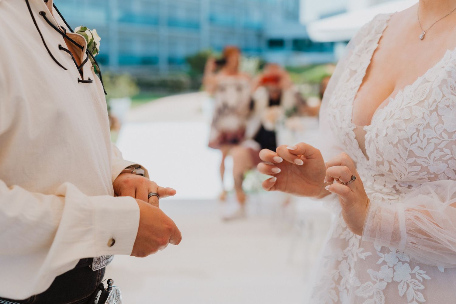 Close-up shot of hands exchanging wedding rings at an outdoor seaside ceremony.