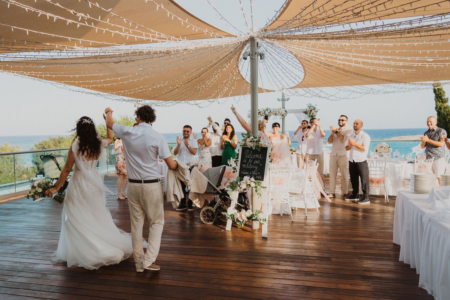 Guests celebrating at seaside wedding reception under golden fabric canopy.