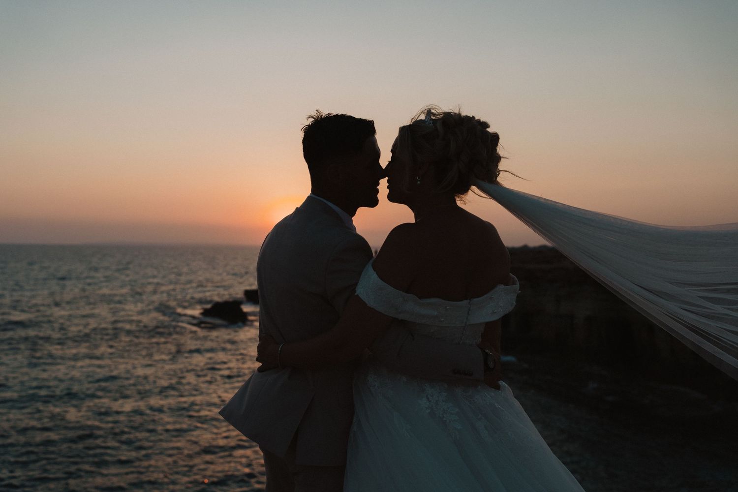 Romantic silhouette of a couple embracing at sunset by the ocean.