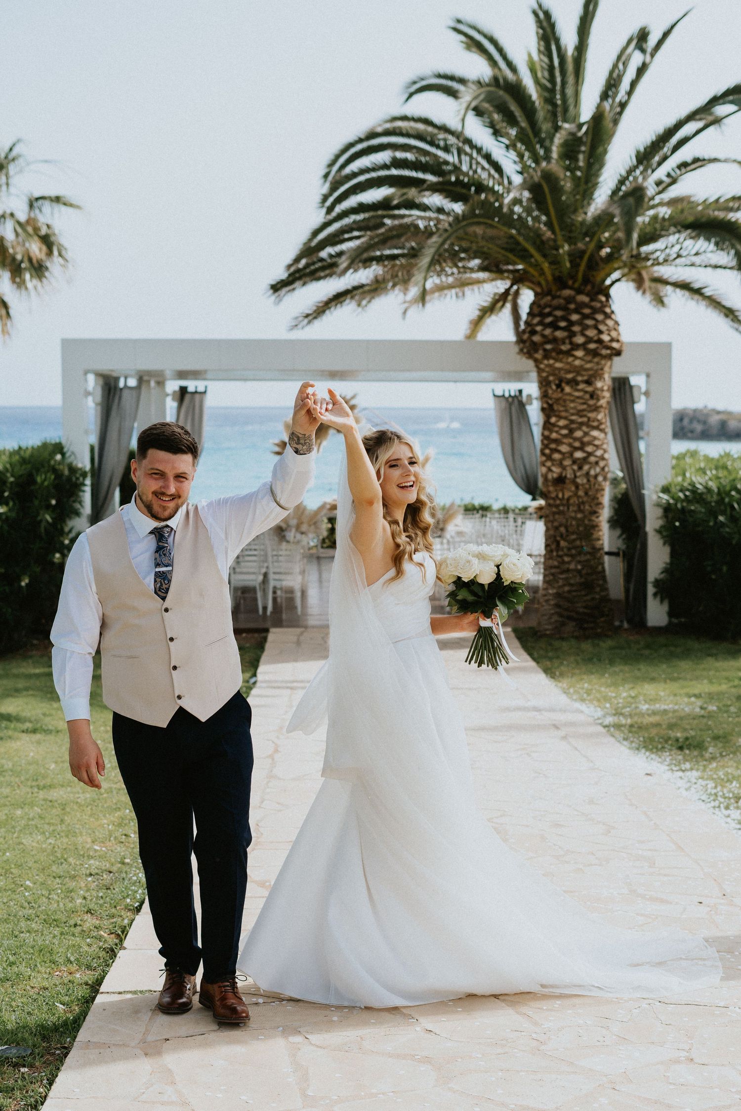 Newlyweds celebrate during their tropical beach wedding ceremony with palm trees and ocean views in the background.