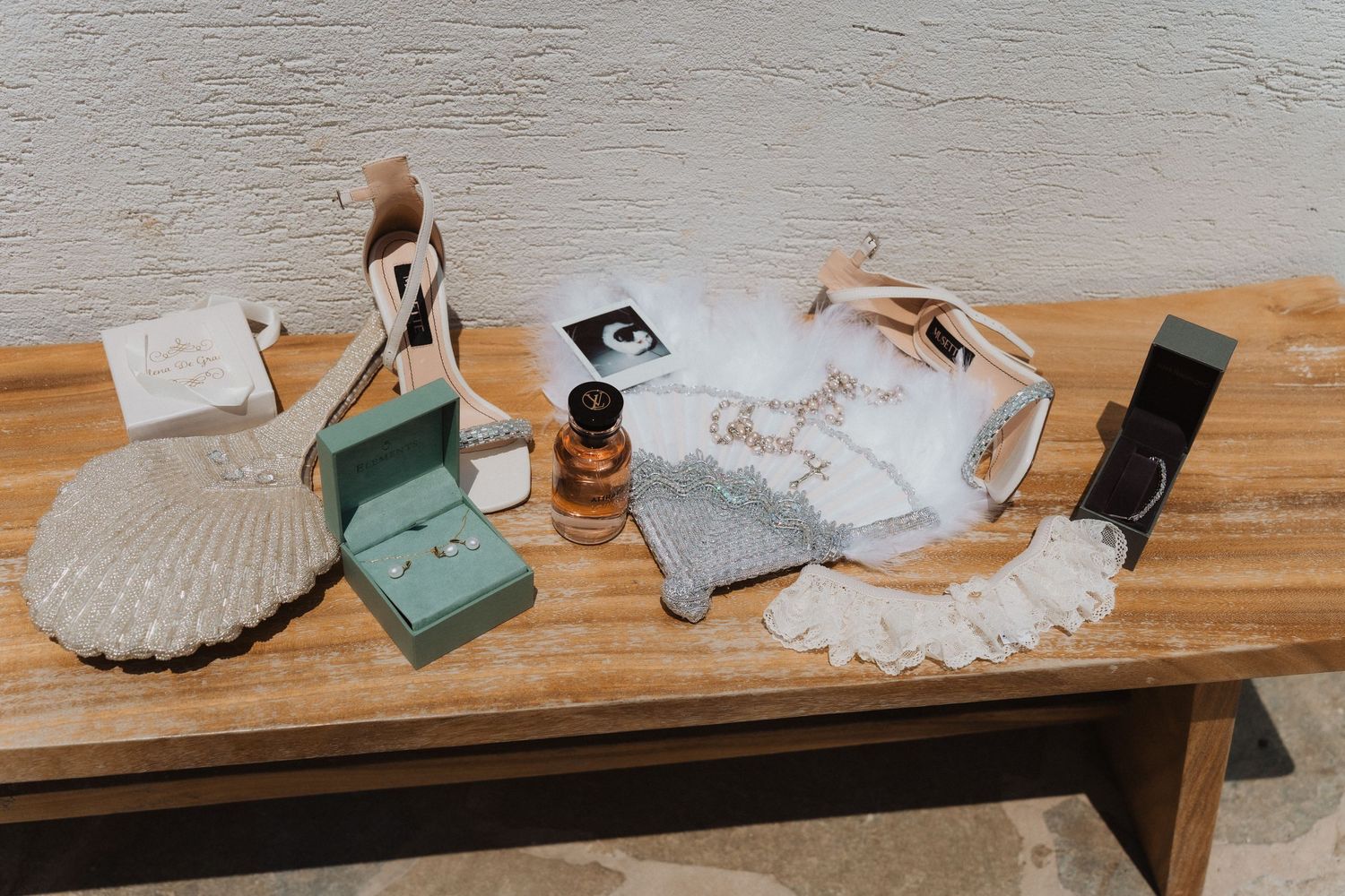 Bridal accessories flat lay on wooden bench featuring rings, perfume, heels, jewelry, and elegant details.