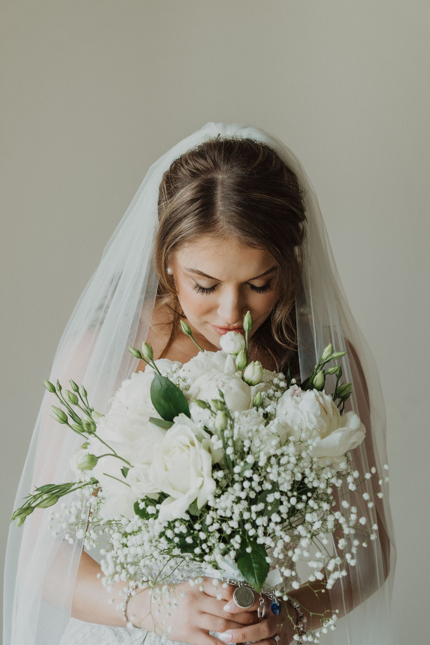 Bride in white veil smelling a bouquet of white roses and baby's breath on her wedding day.